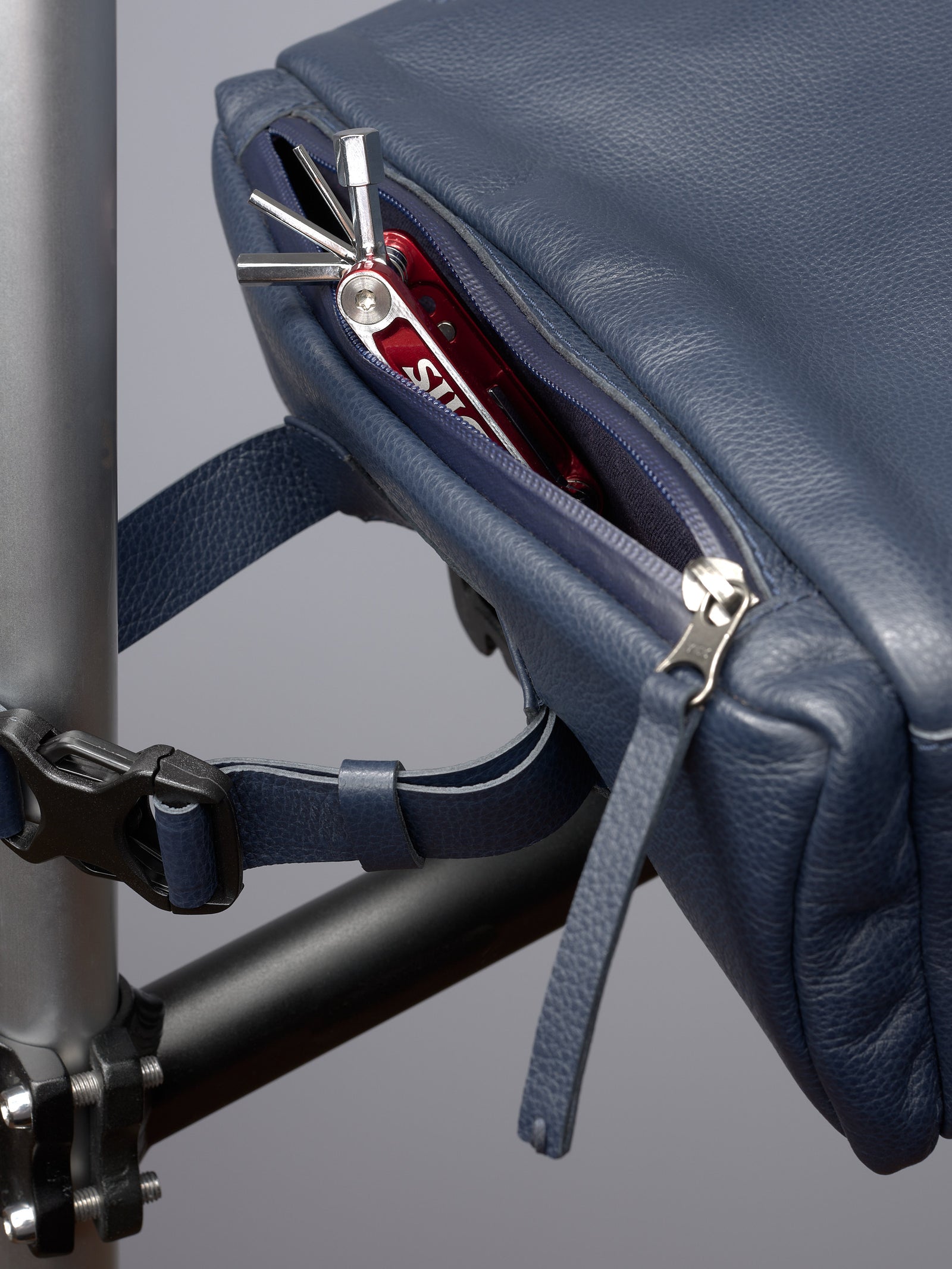 Close-up of the blue leather bike bag's zippered side pocket holding a small red bicycle repair multi-tool.
