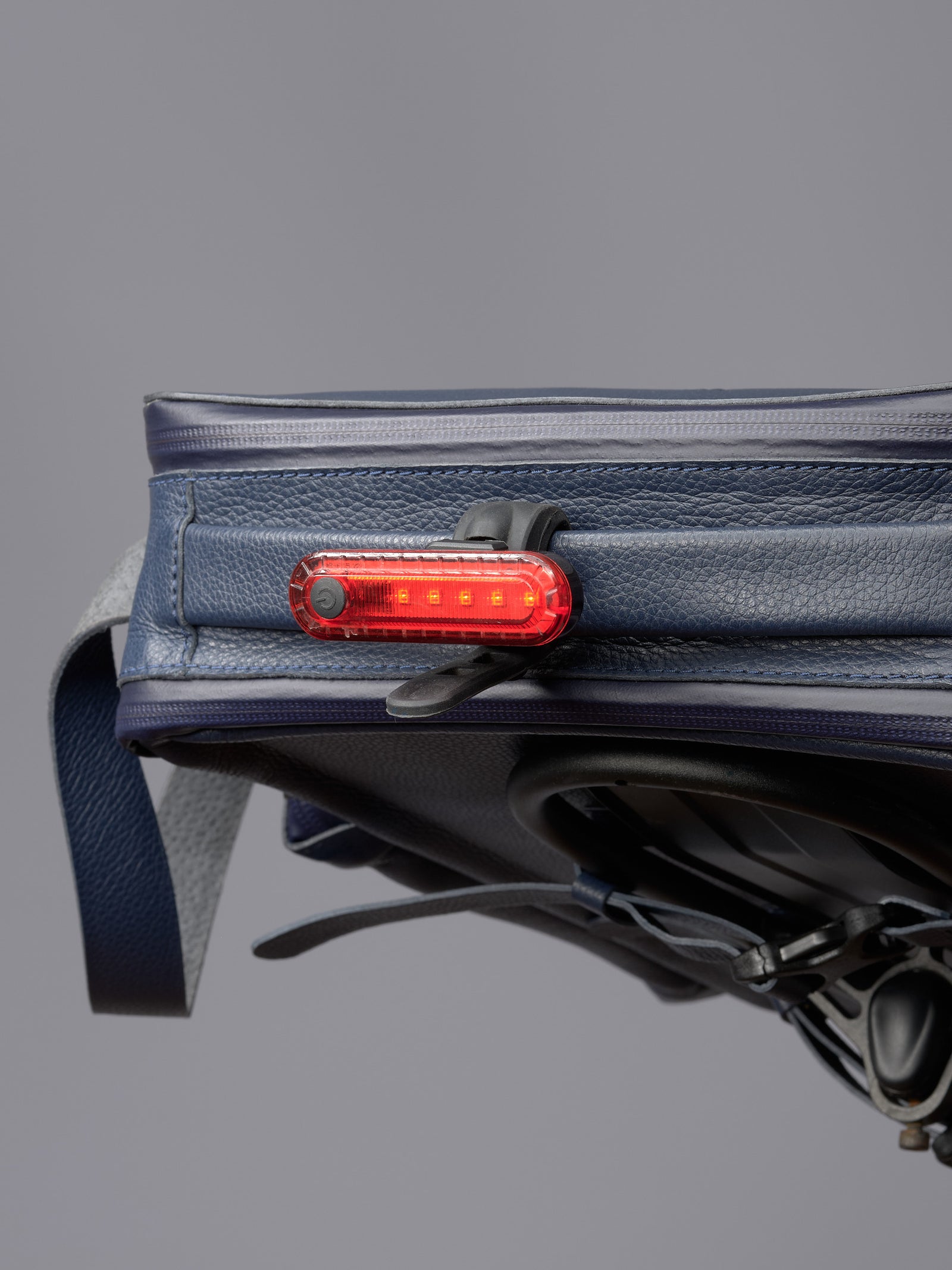 Detail of the blue Capra Leather bag on a bike with a clip-on red LED light for cyclist visibility.