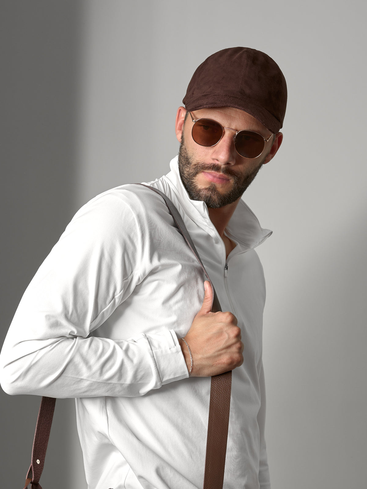 Man wearing a brown suede Capra Leather cap and sunglasses with a white shirt.