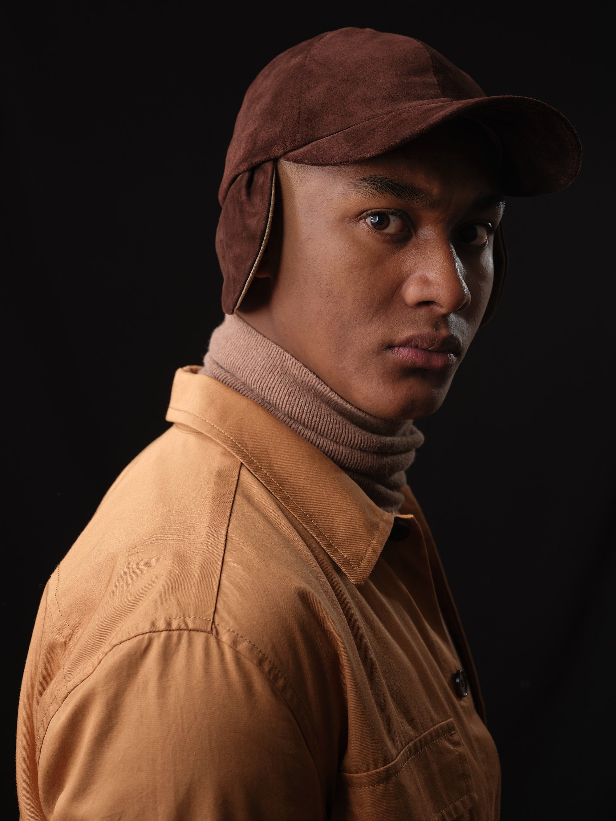 Stylish man wearing a brown suede baseball cap with ear flaps by Capra Leather 