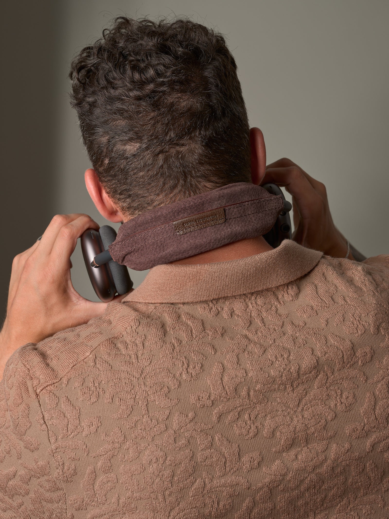 Rear view of a man putting on headphones with a brown Capra Leather headband cover.