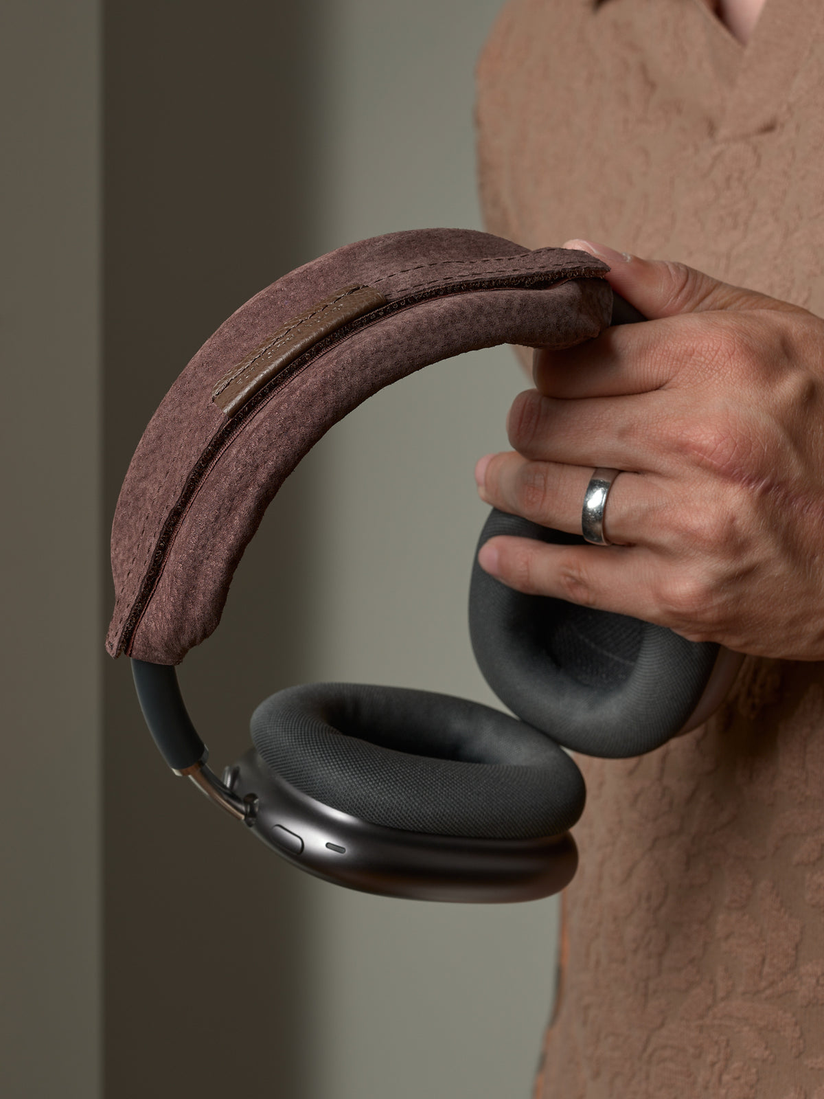 Close-up of a man holding headphones with a brown Capra Leather headband cover.
