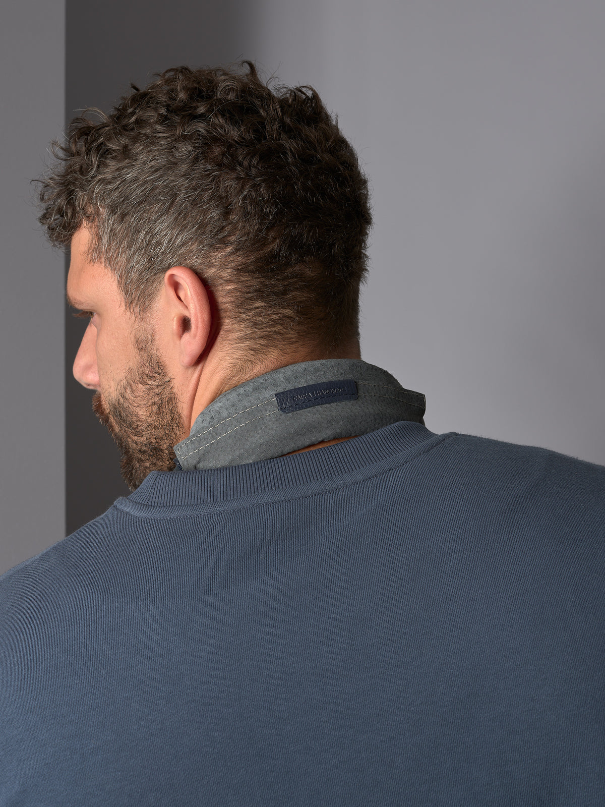 Rear view of a man wearing a blue sweatshirt with a gray Capra Leather headphone headband cover.