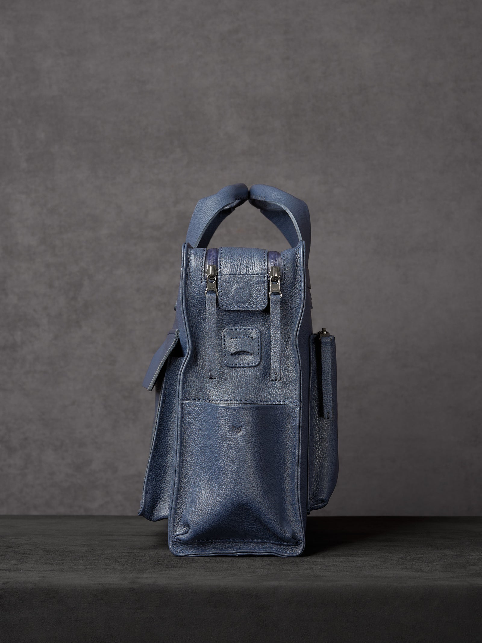 Side view of Capra Leather navy blue messenger bag showing zippered side pocket.