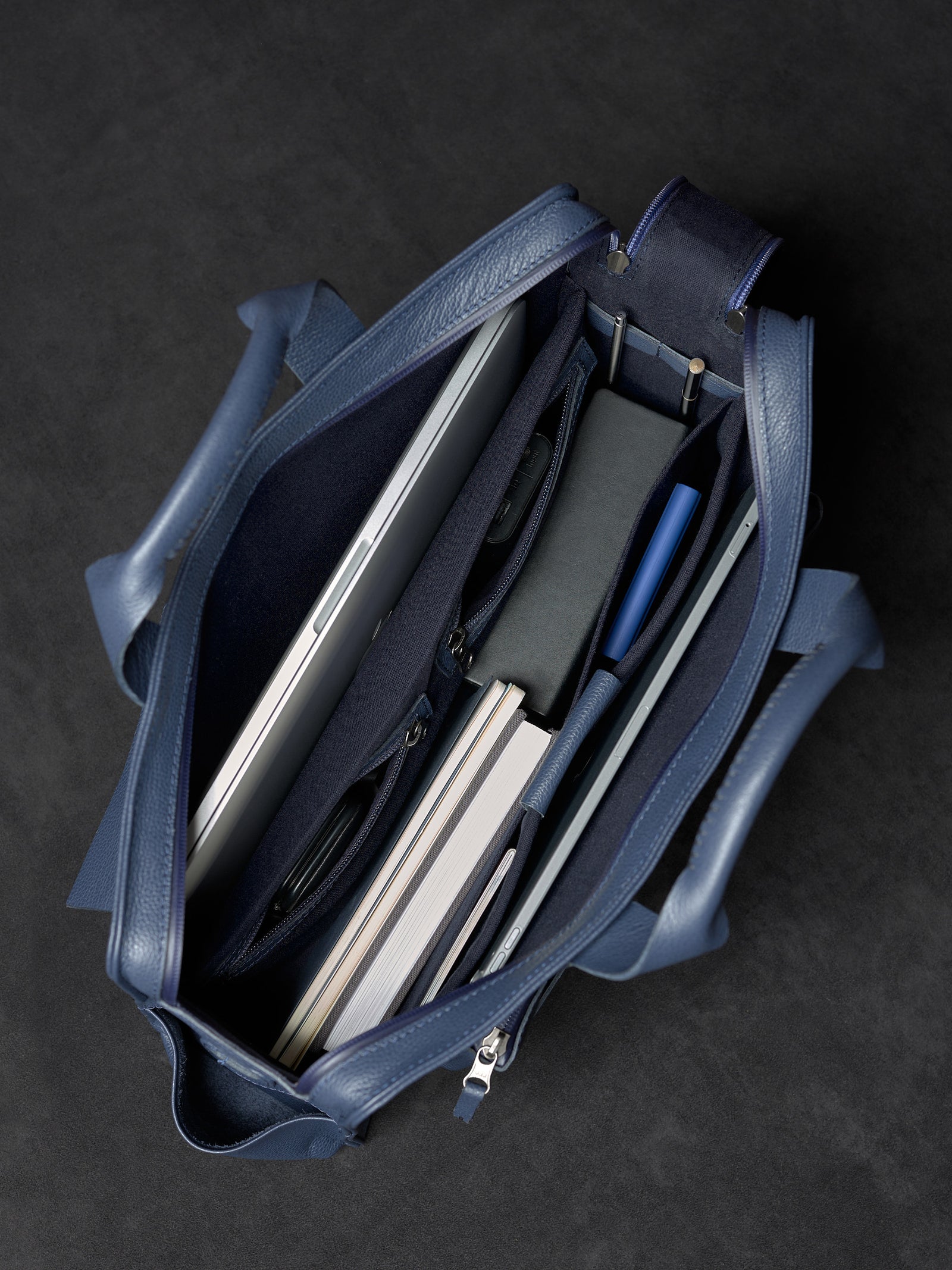 Organized interior of Capra Leather navy briefcase filled with a laptop and notebook.