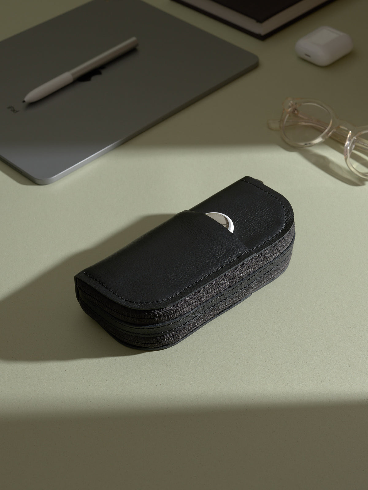 Closed black leather double-glasses case resting on a desk with a laptop and other personal accessories.