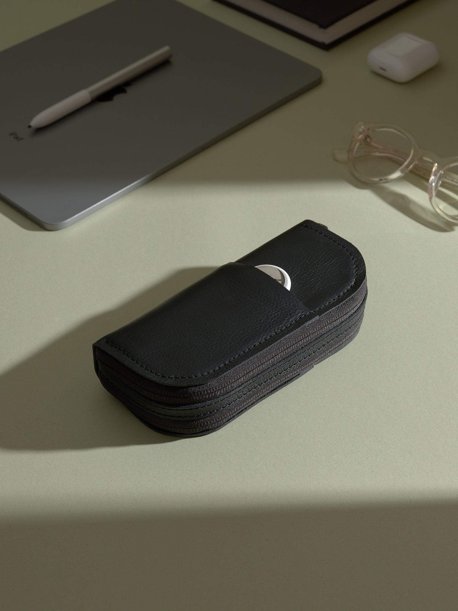 Closed black leather double-glasses case resting on a desk with a laptop and other personal accessories.