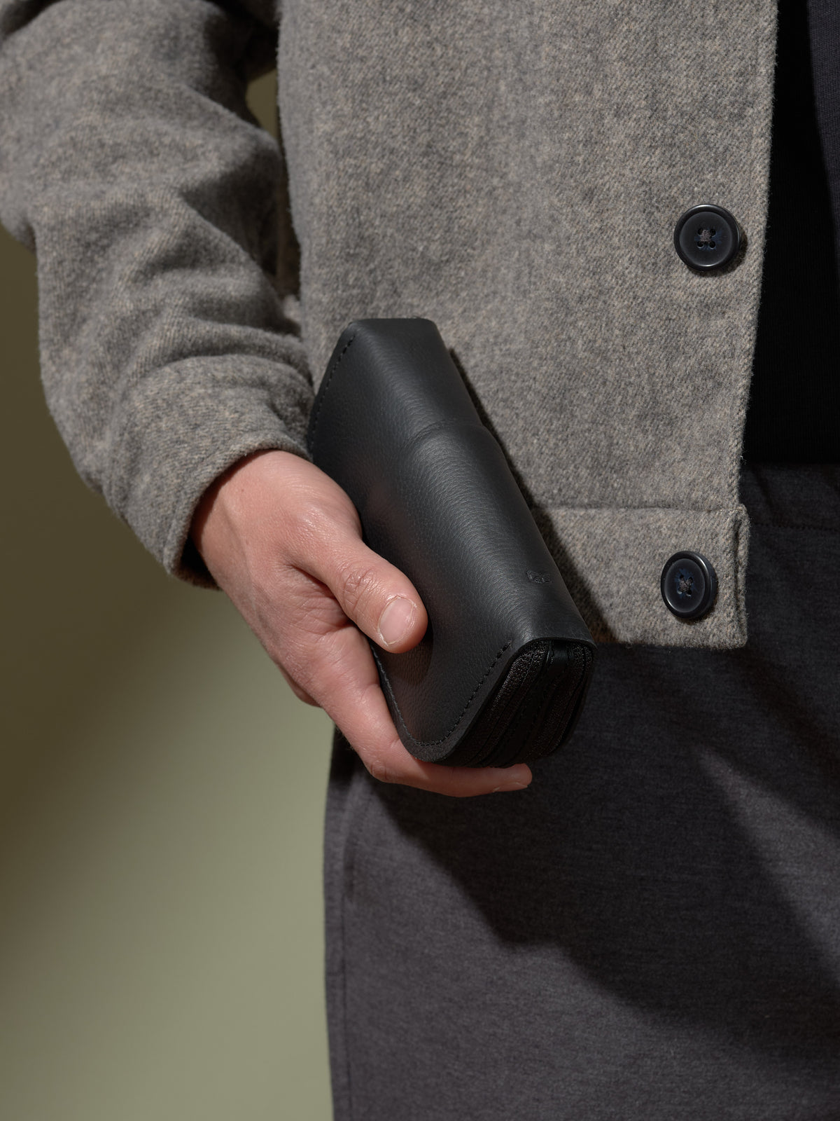 Man holding the compact, closed black leather double-glasses case, showing its premium zippered finish.