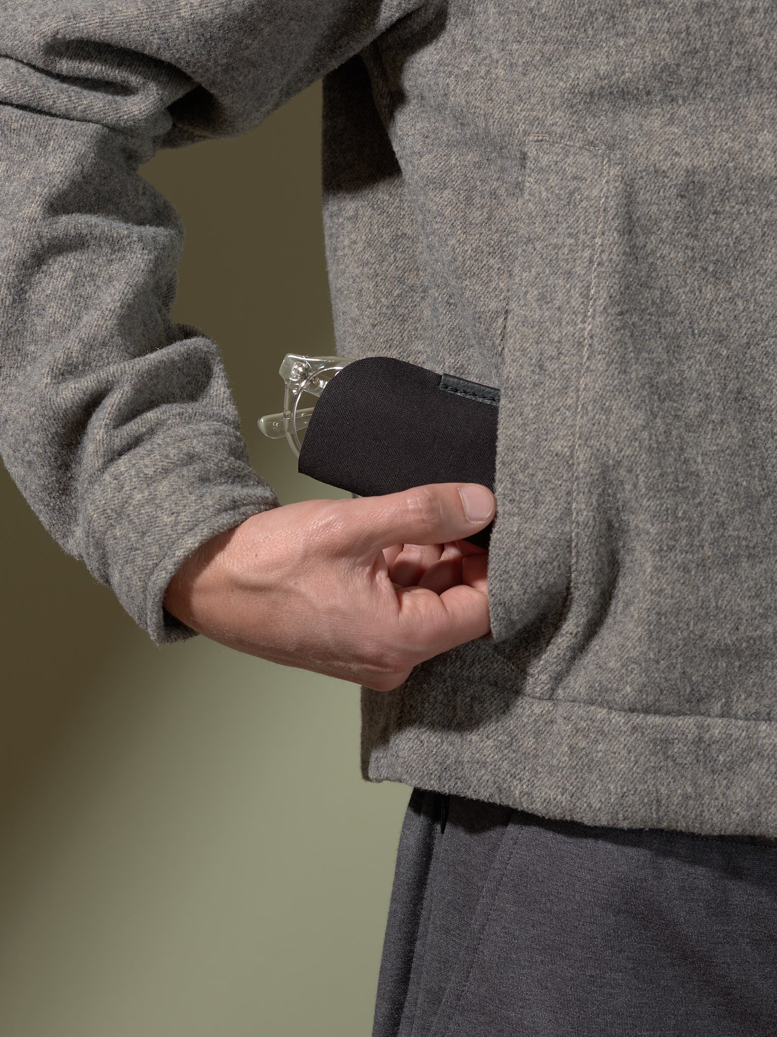 Man's hand placing the soft internal pouch of the black leather double-glasses case into a jacket pocket.