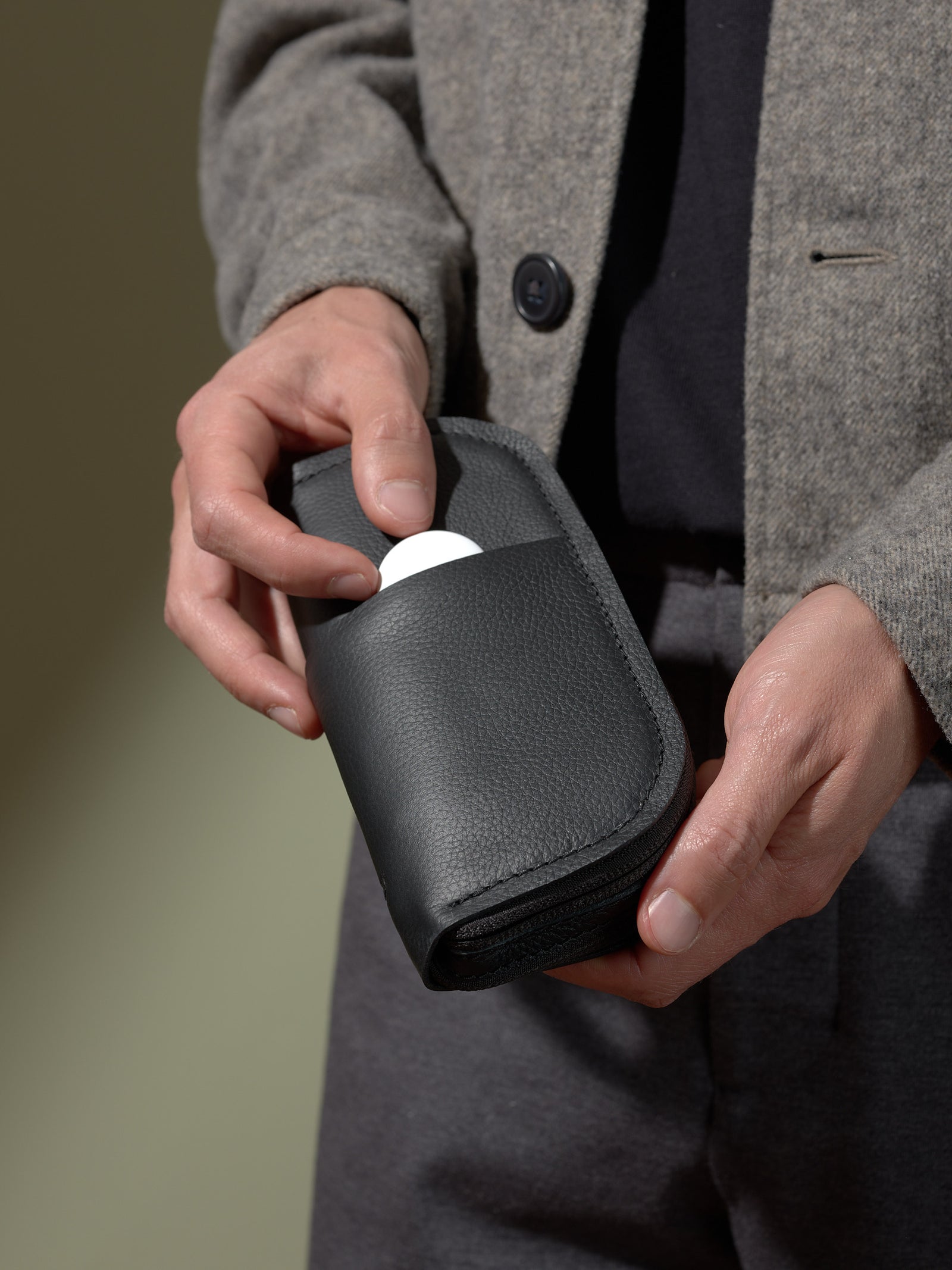 Man retrieving a small item from the accessory slip pocket of the black leather double-glasses case.