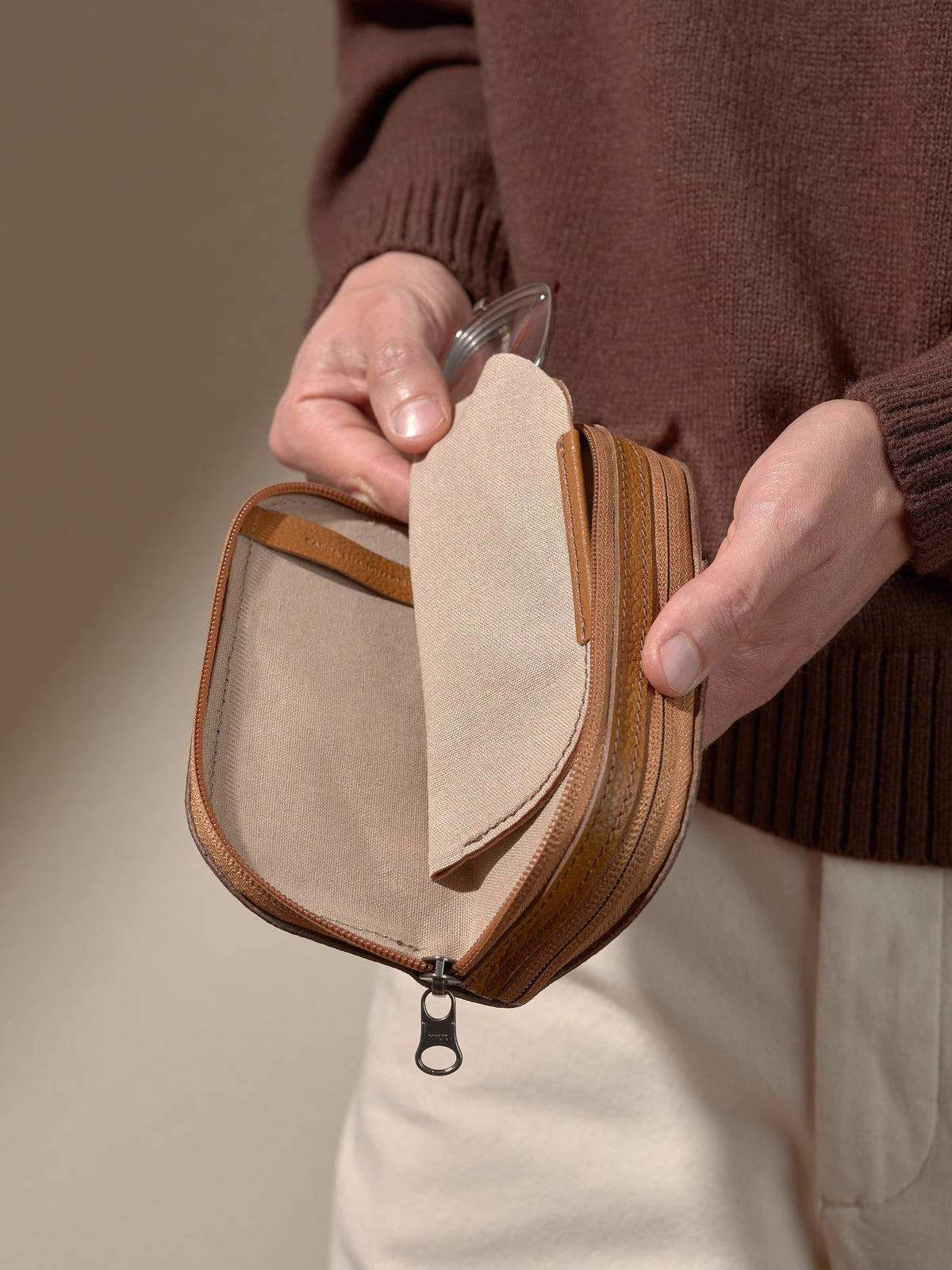 Close-up of a person's hands holding the open tan leather double glasses case, revealing one inner soft fabric sleeve partially pulled out.