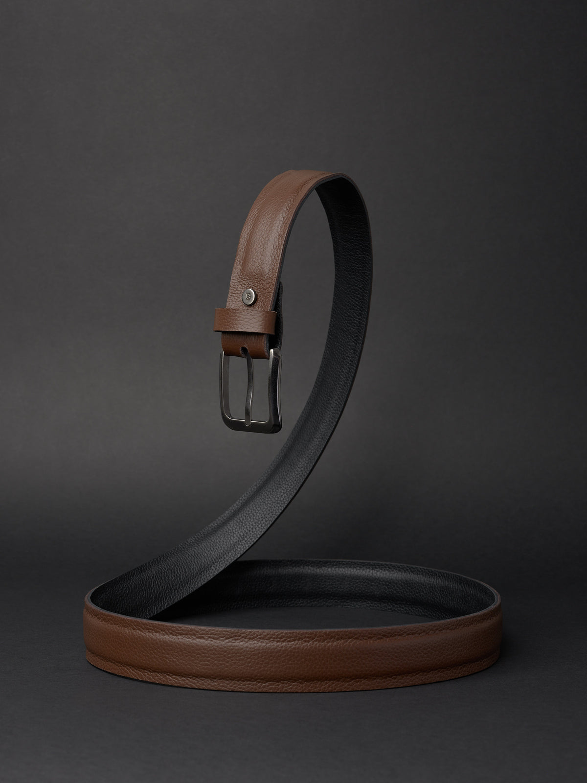 Handcrafted 32mm reversible leather belt in brown and black with a gunmetal buckle on a dark studio background.