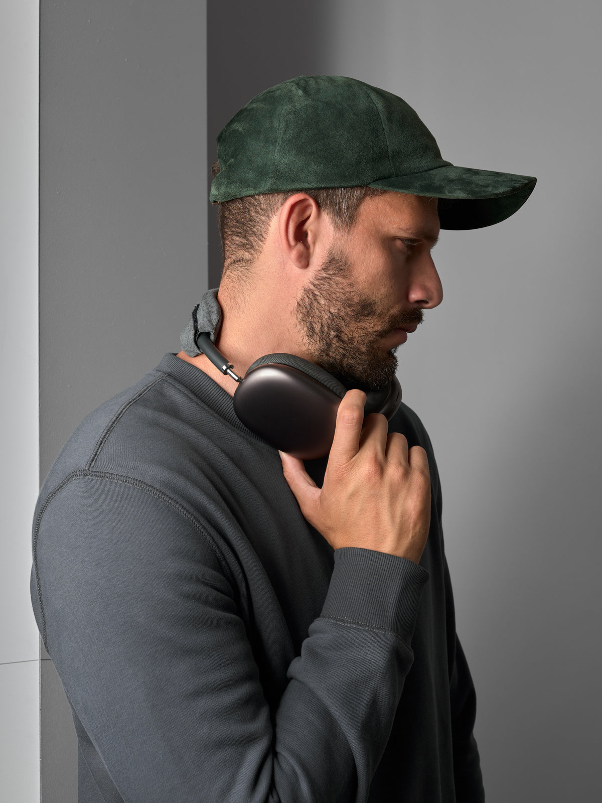 Man in a green suede Capra Leather cap holding black headphones around his neck.