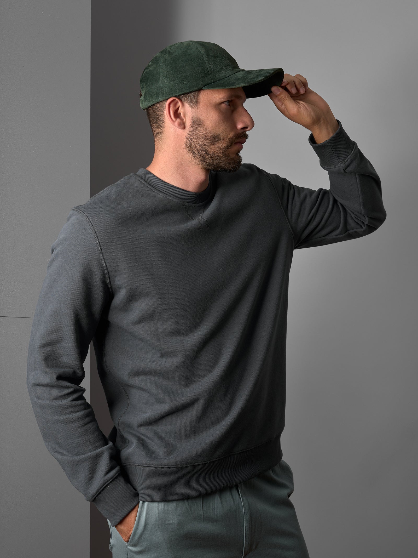 Man wearing a green suede Capra Leather cap with a gray sweatshirt and light-colored pants.