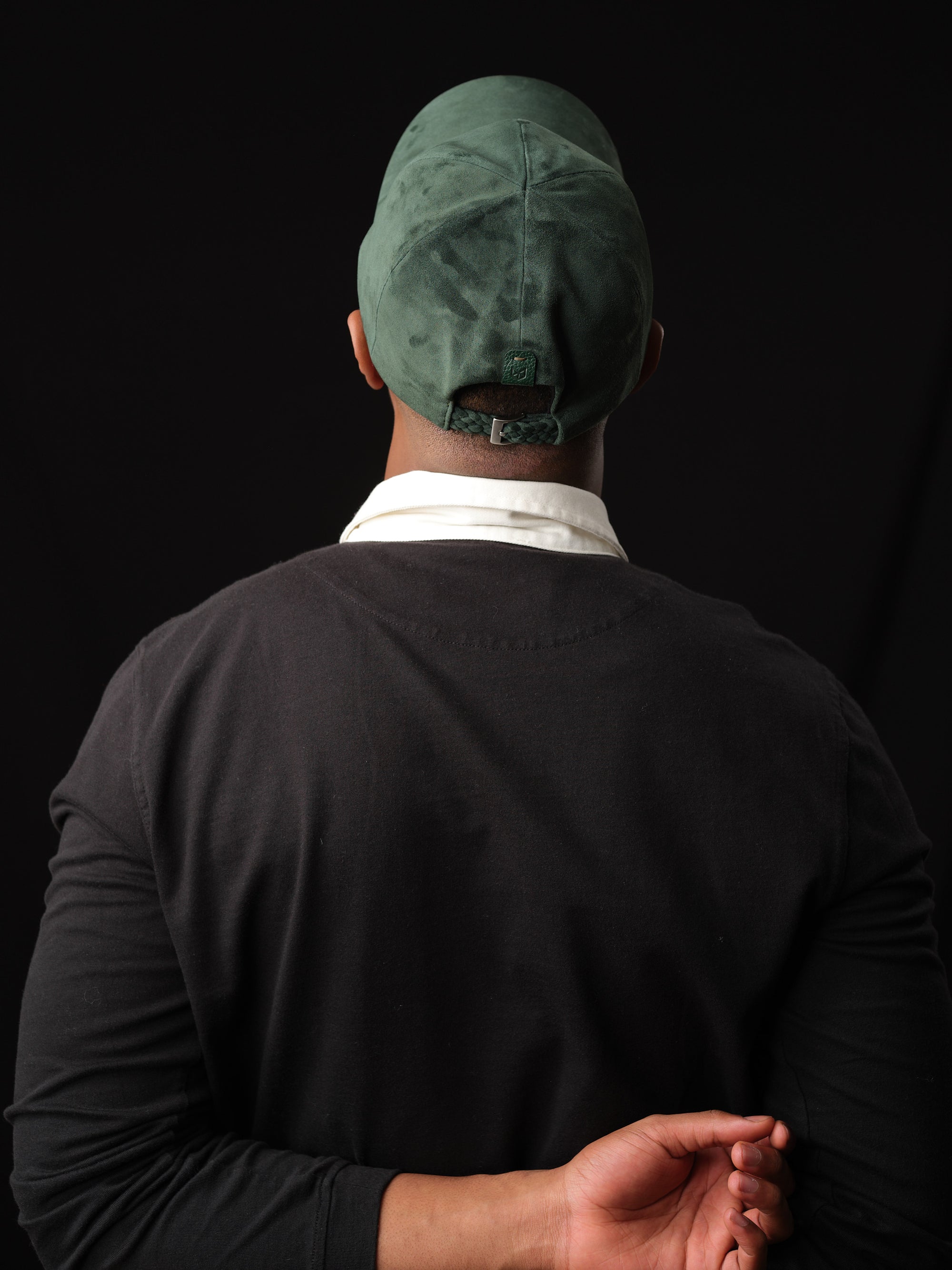 Man wearing a green suede baseball cap with ear flaps, handcrafted by Capra Leather