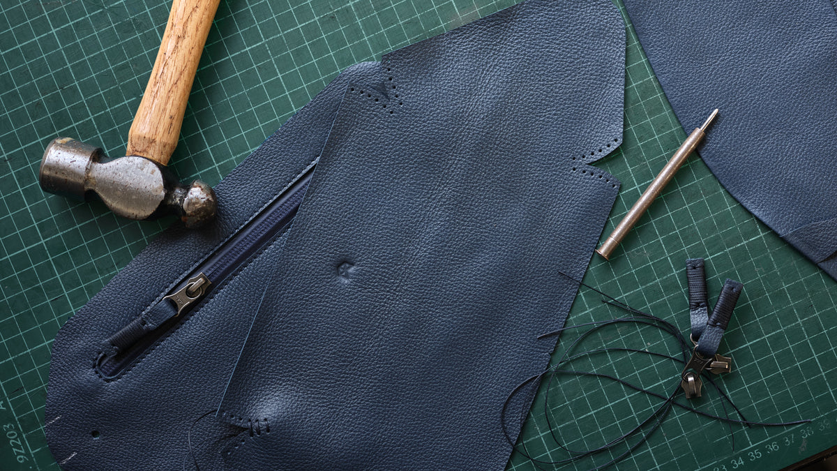 Cut leather pieces, a hammer and an awl on a cutting mat in the Capra Leather studio
