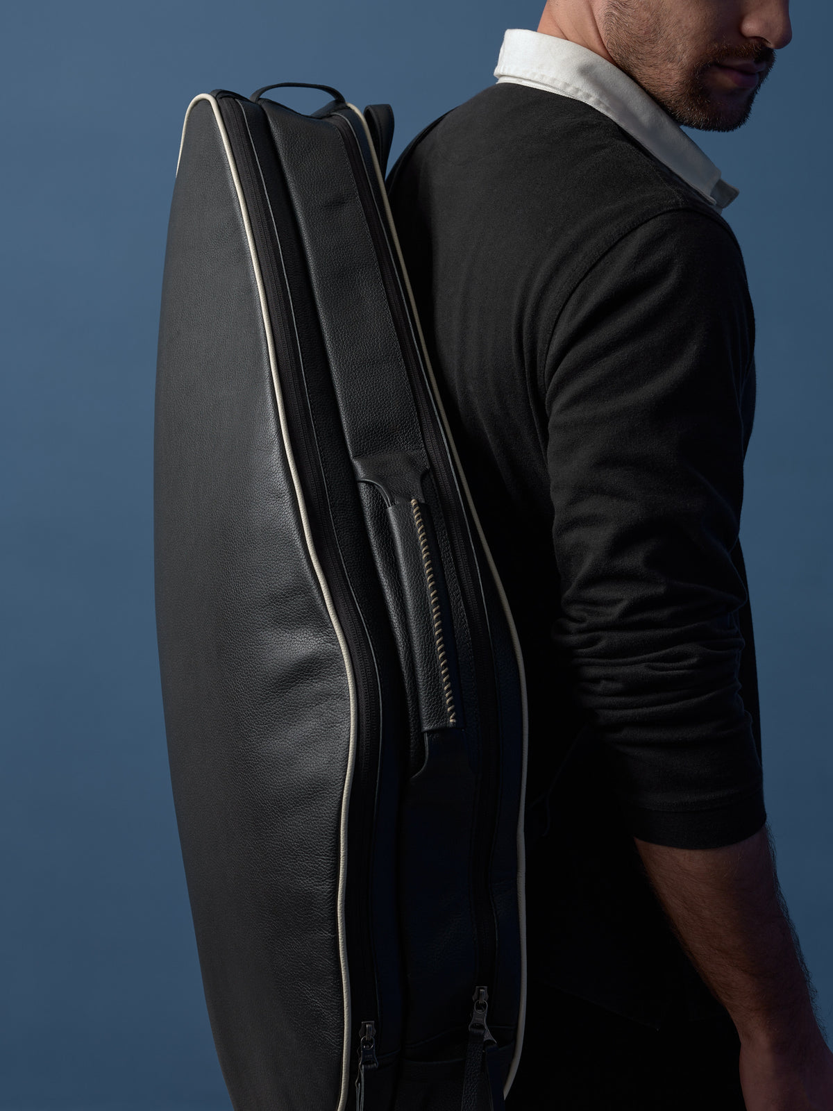 Detailed side view of the cream piping and artisan stitching on a black leather tennis backpack.