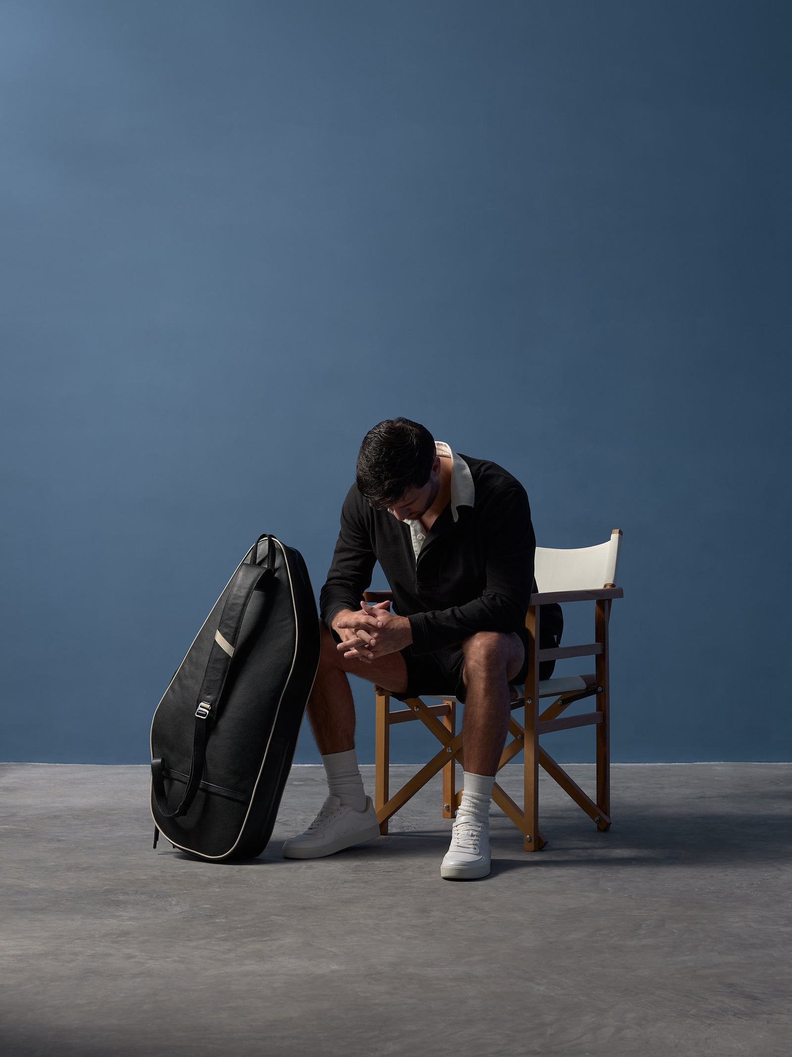 Man wearing a premium black leather tennis backpack with cream piping against a blue background.