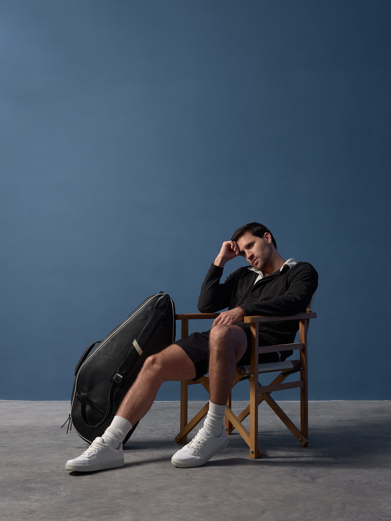Lifestyle shot of a designer leather tennis bag leaning against a classic courtside chair.