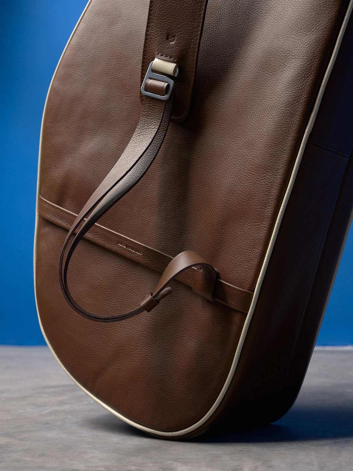 Detail of the adjustable brown leather strap on a tennis bag, featuring a metal buckle and cream leather accents.