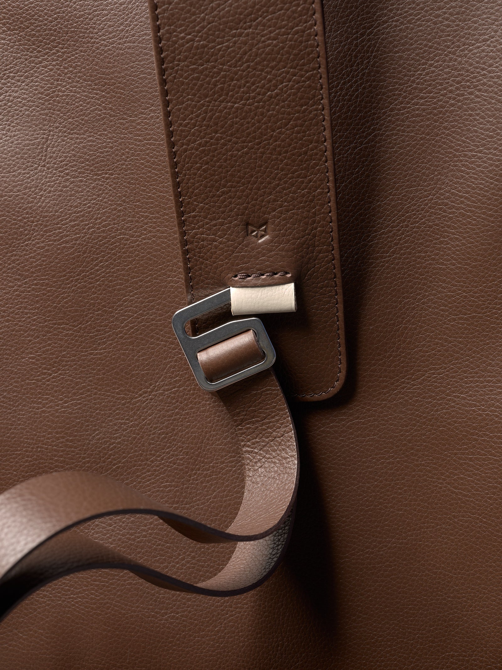 Extreme close-up of a premium leather tennis bag strap, highlighting the embossed logo and pebbled grain texture.