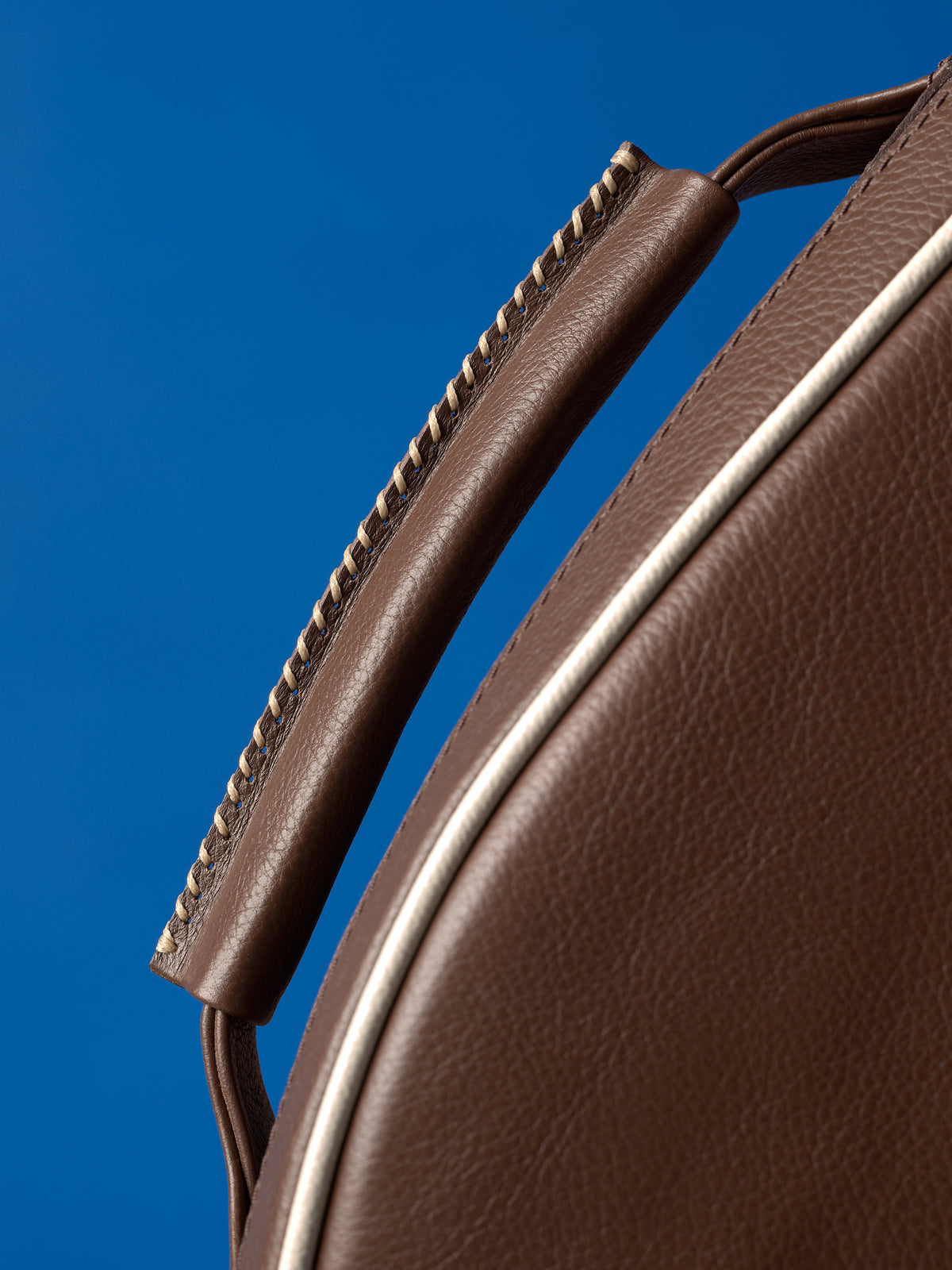 Close-up of the hand-stitched leather handle on a tennis bag, highlighting the cream-colored thread and craftsmanship.