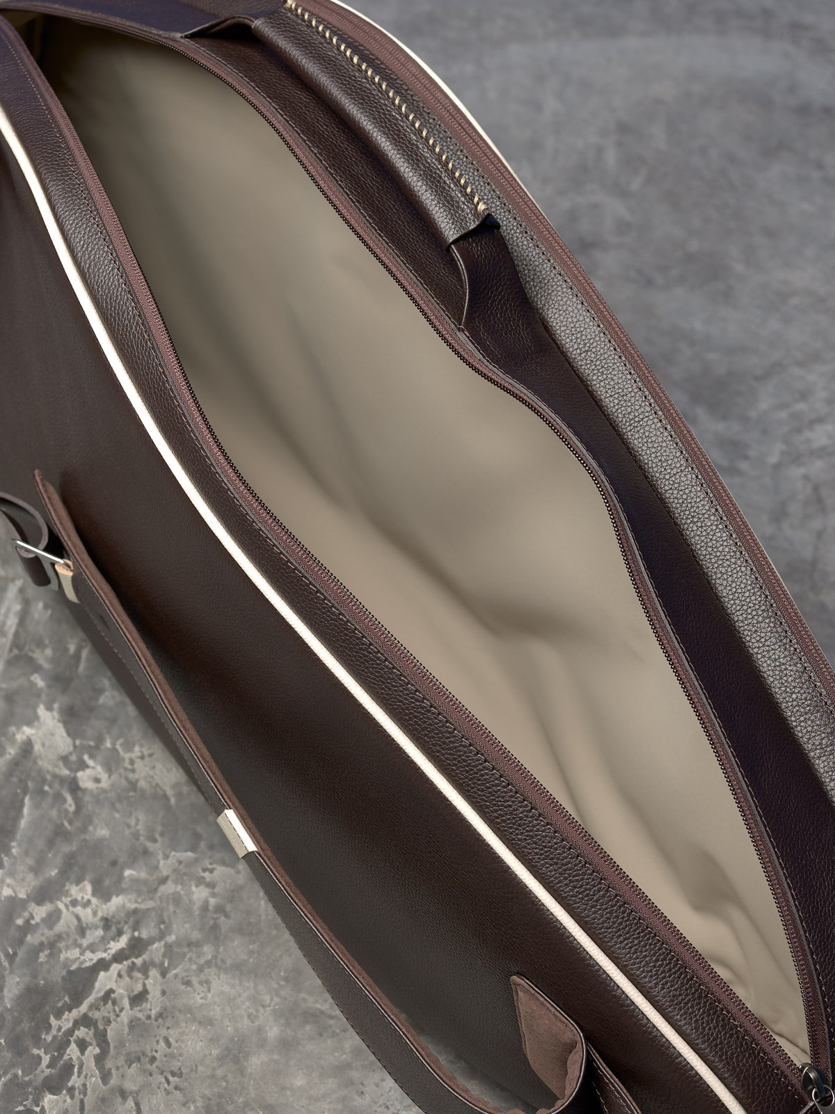 A close-up, angled view of an opened dark brown leather bag, revealing a clean, light-colored fabric interior lining.