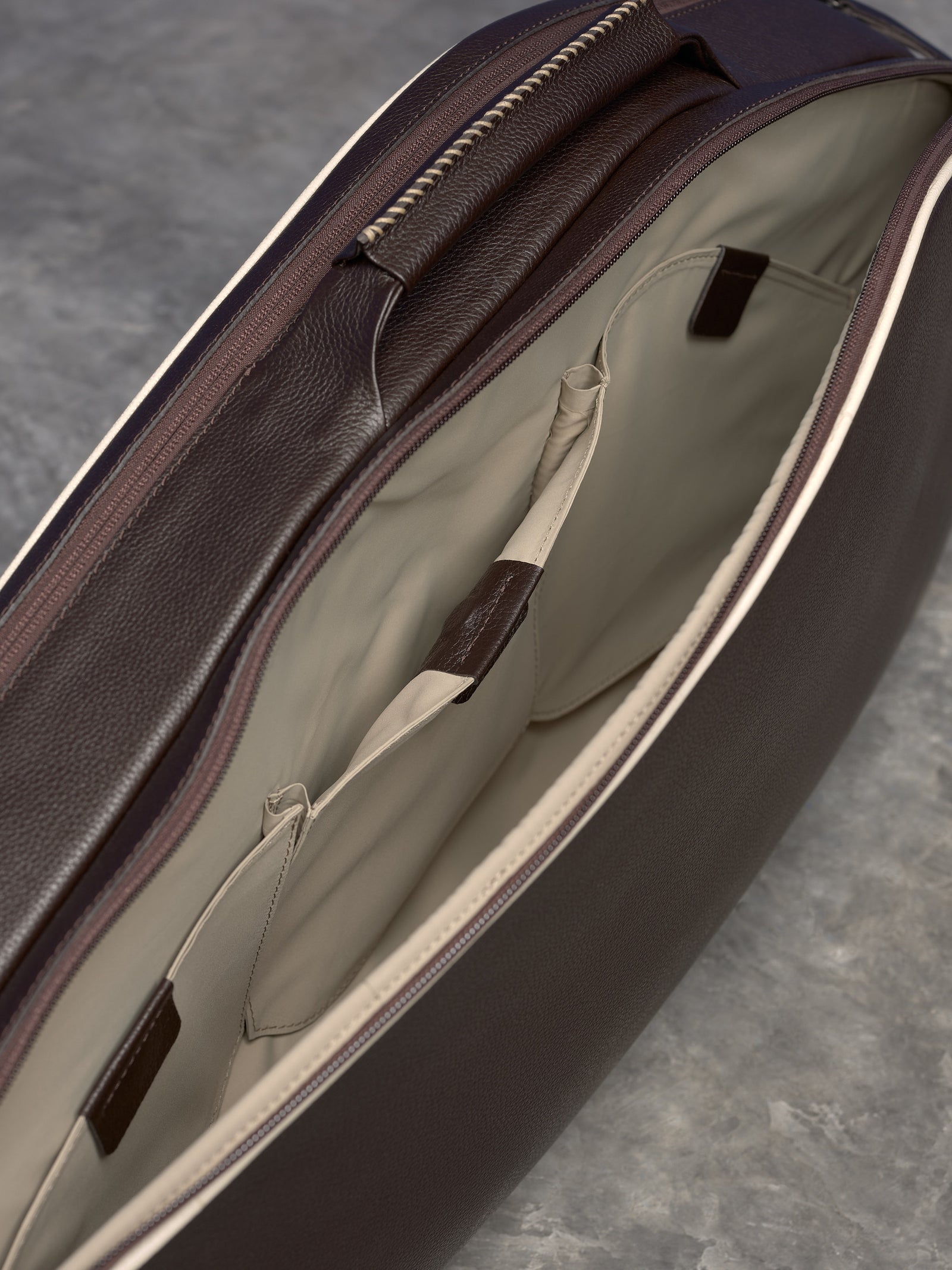 Detailed overhead view of an opened brown leather bag showing the light-beige fabric lining and multiple internal organizational pockets.
