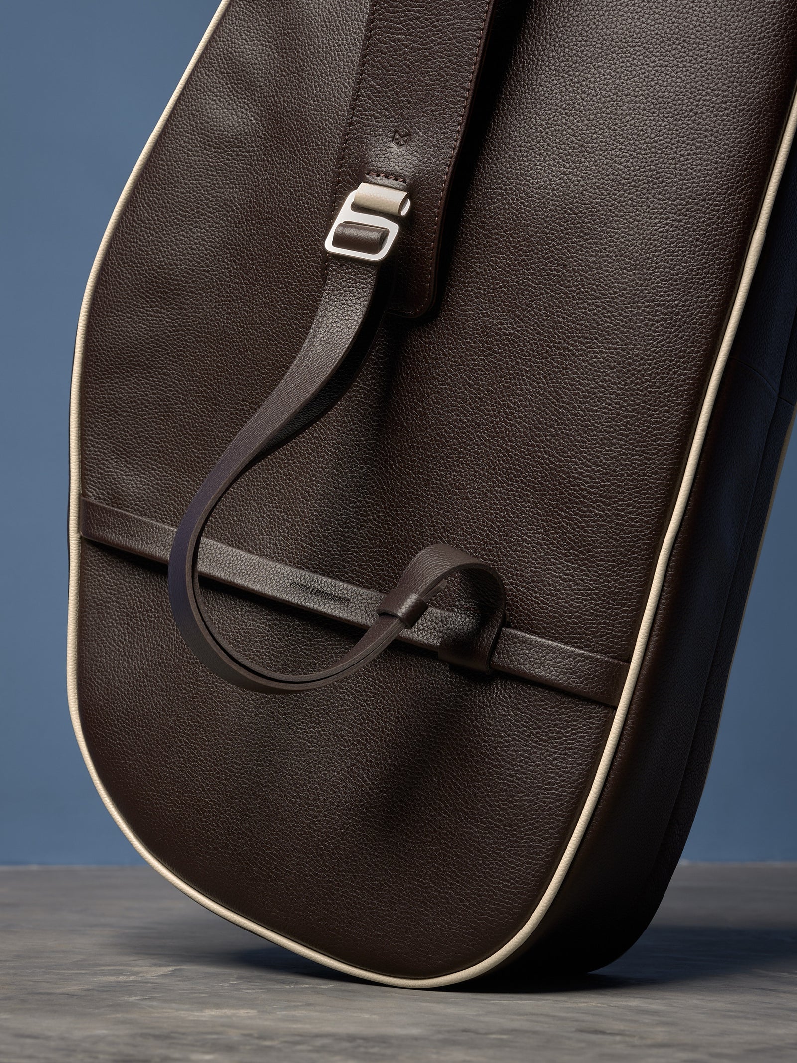 Detailed view of the rear of a brown pebbled leather bag, highlighting the white trim, adjustable shoulder strap, and polished metal buckle.