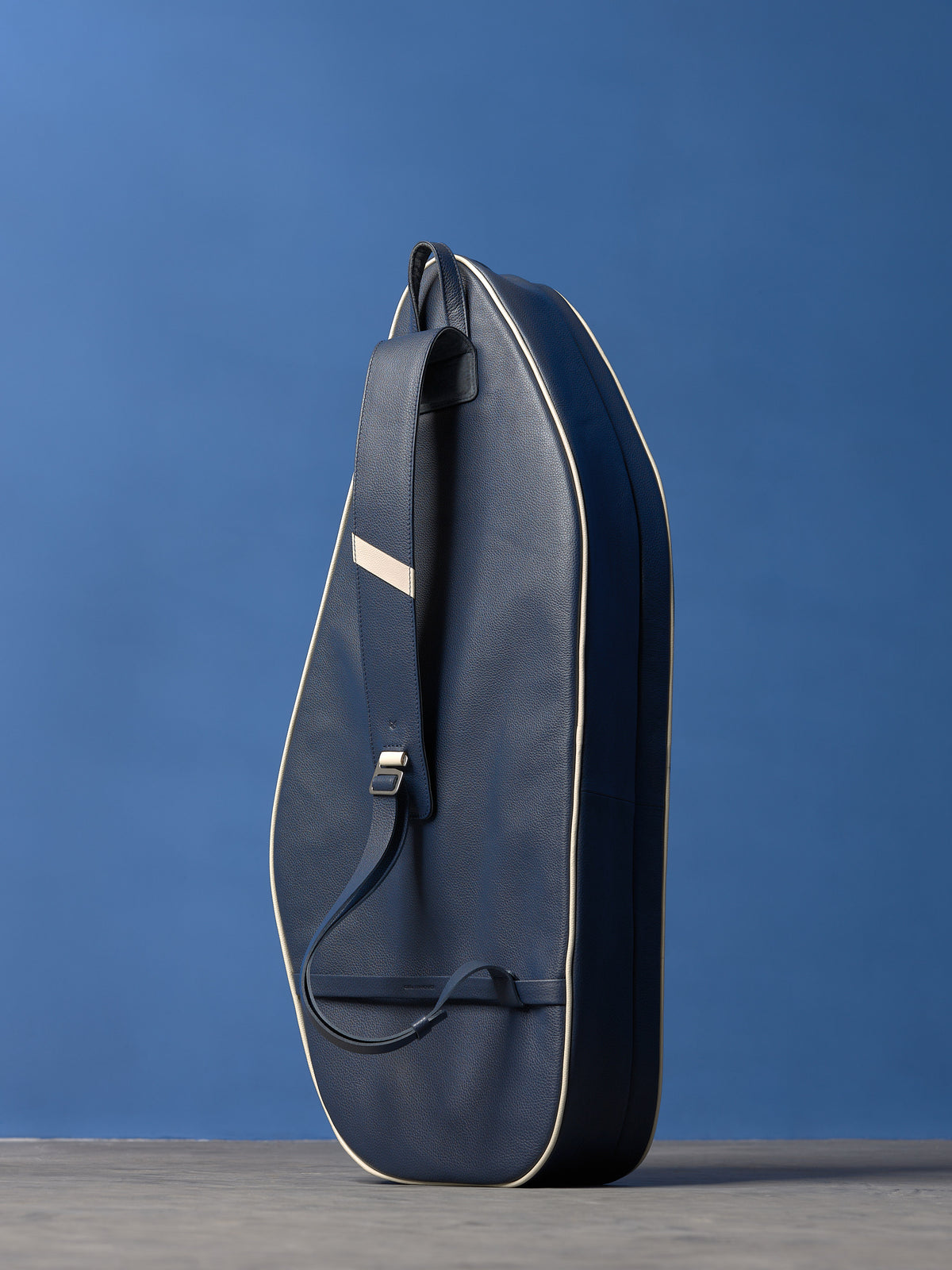 Navy blue full-grain leather tennis racket bag with white piping and a wide adjustable shoulder strap.
