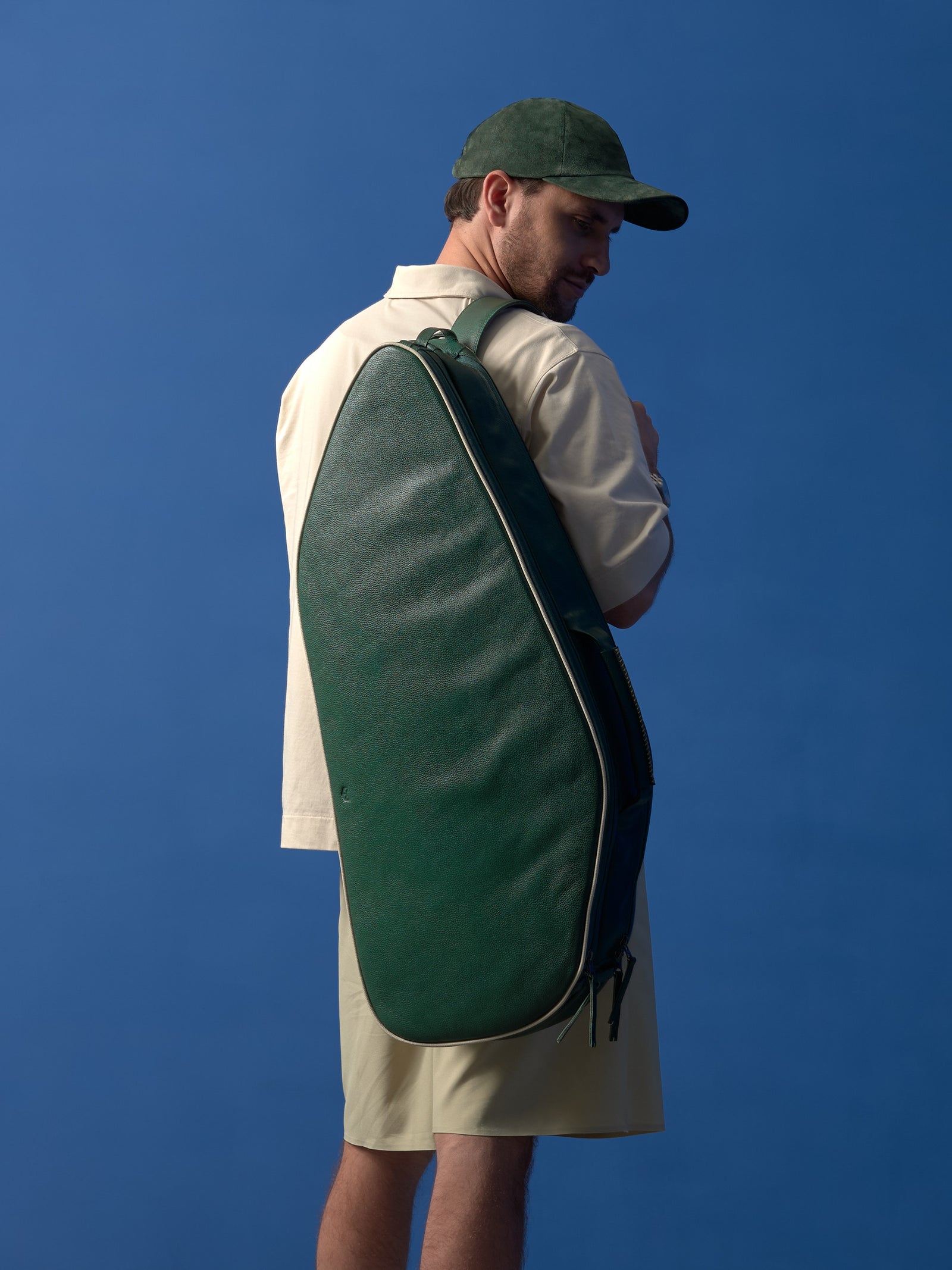 A man wearing the green leather tennis bag over his shoulder, showing the bag in a functional, hands-free context.