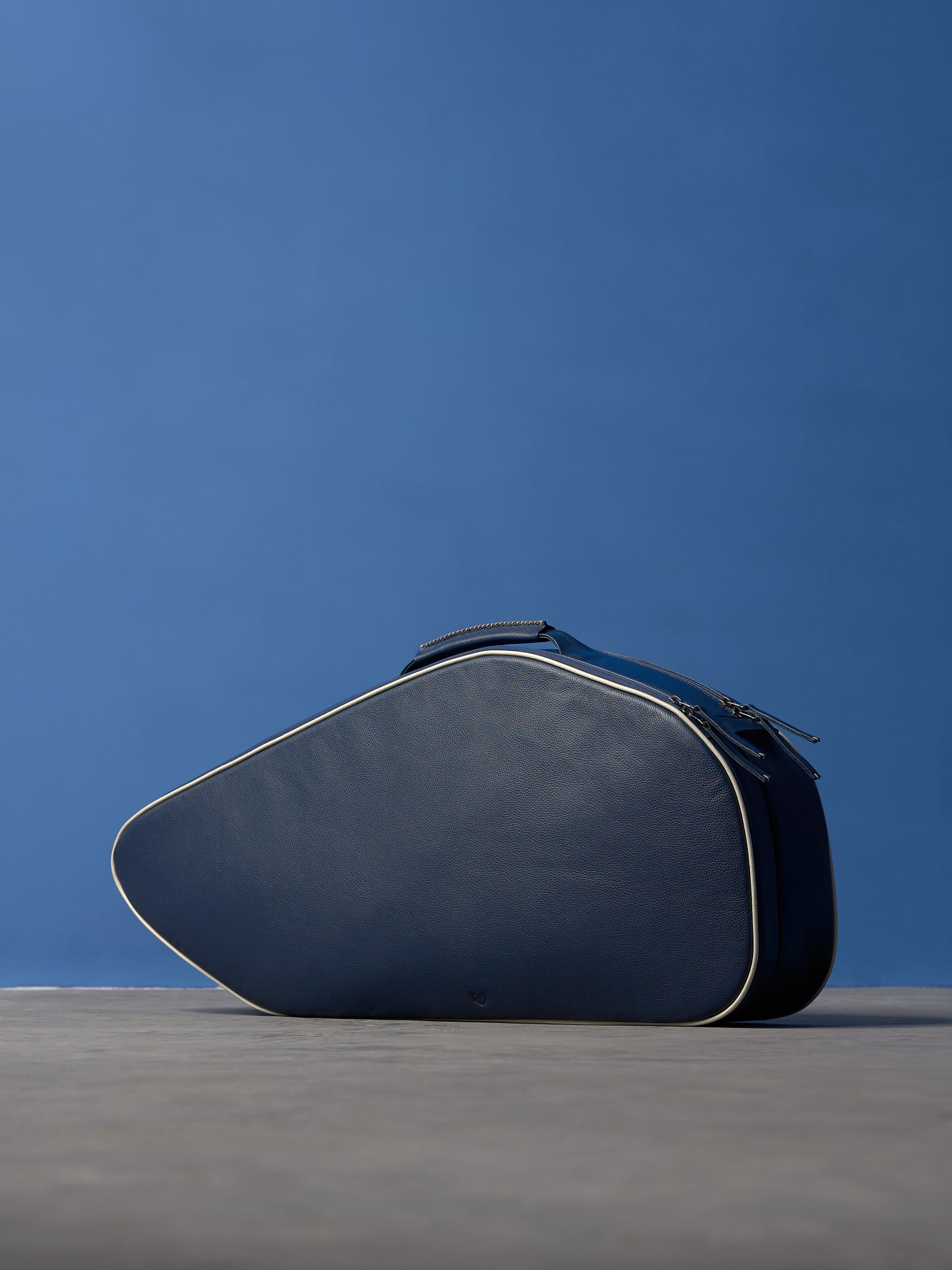 Navy blue full-grain leather tennis racket bag with white piping and a wide adjustable shoulder strap.