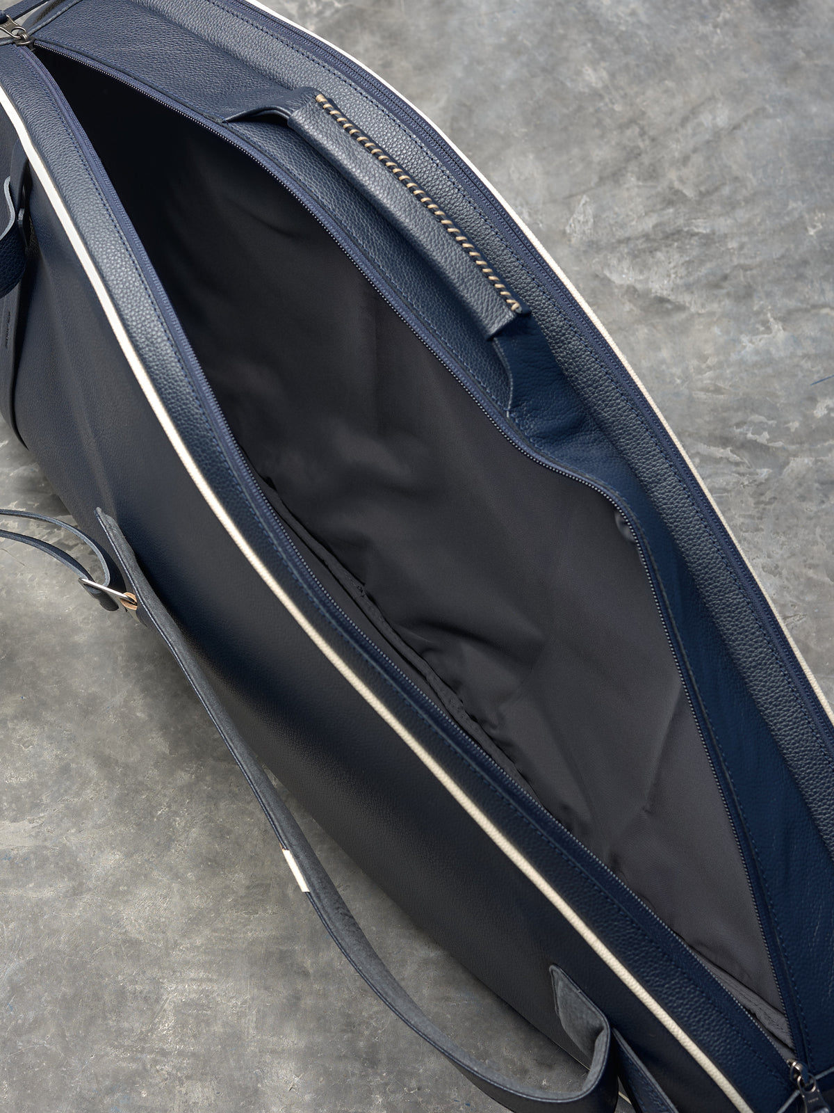 Open view of a luxury leather tennis bag showing the dark gray fabric lining and spacious main compartment.