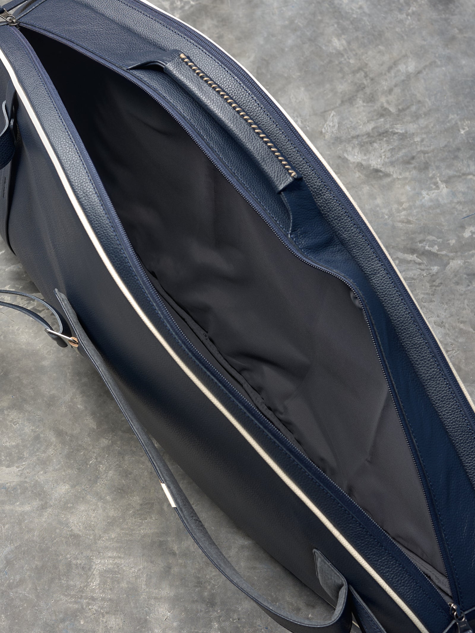 Open view of a luxury leather tennis bag showing the dark gray fabric lining and spacious main compartment.