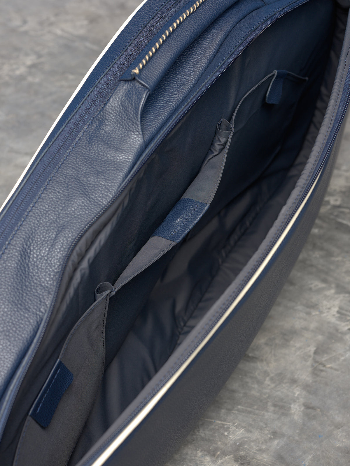 Detailed view of the interior organizer pockets and smooth zipper of a navy leather racket bag.