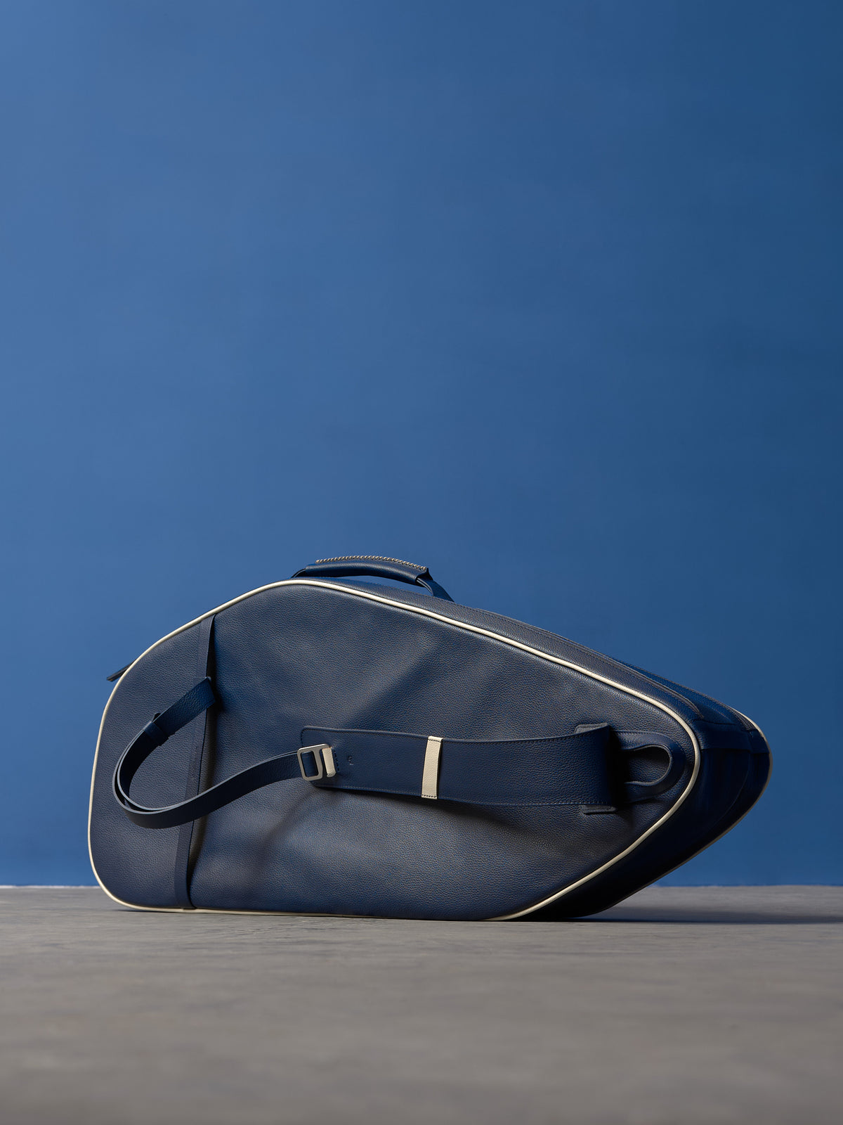 Premium navy leather tennis bag resting on its side, showcasing the ergonomic strap design and clean lines.