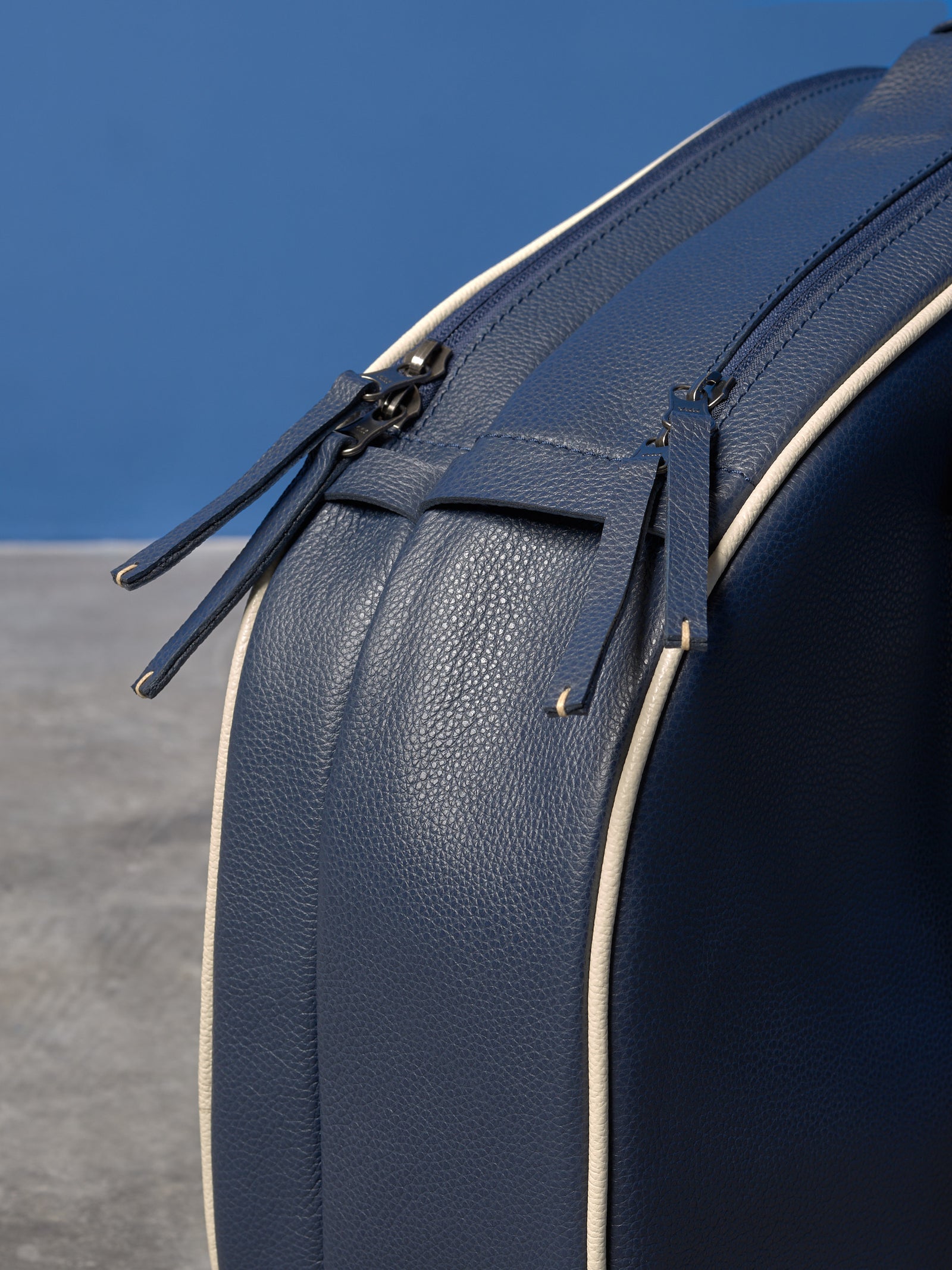 Close-up of double metal zippers with navy leather pulls and contrasting cream piping on a racket bag.