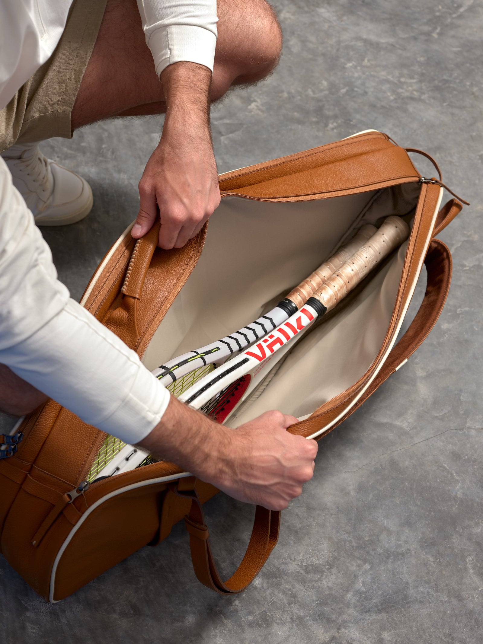 Top-down view of the interior of a luxury leather tennis bag containing two Volkl tennis rackets.
