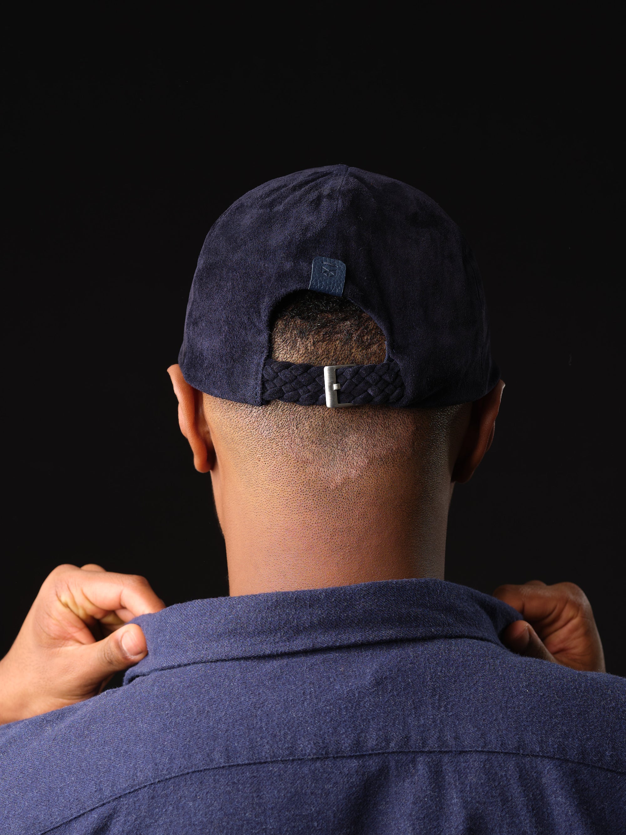 Back view of a navy suede baseball cap with braided strap and buckle by Capra Leather