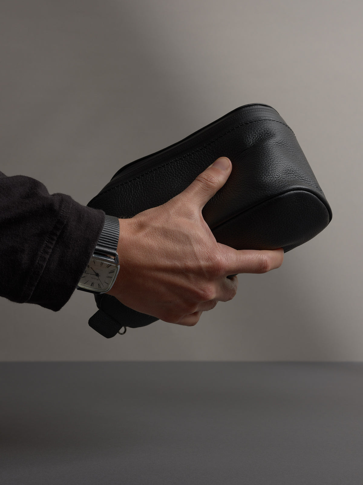 Close-up of a man&#39;s hand holding the black full-grain leather Capra dopp kit, showing texture.