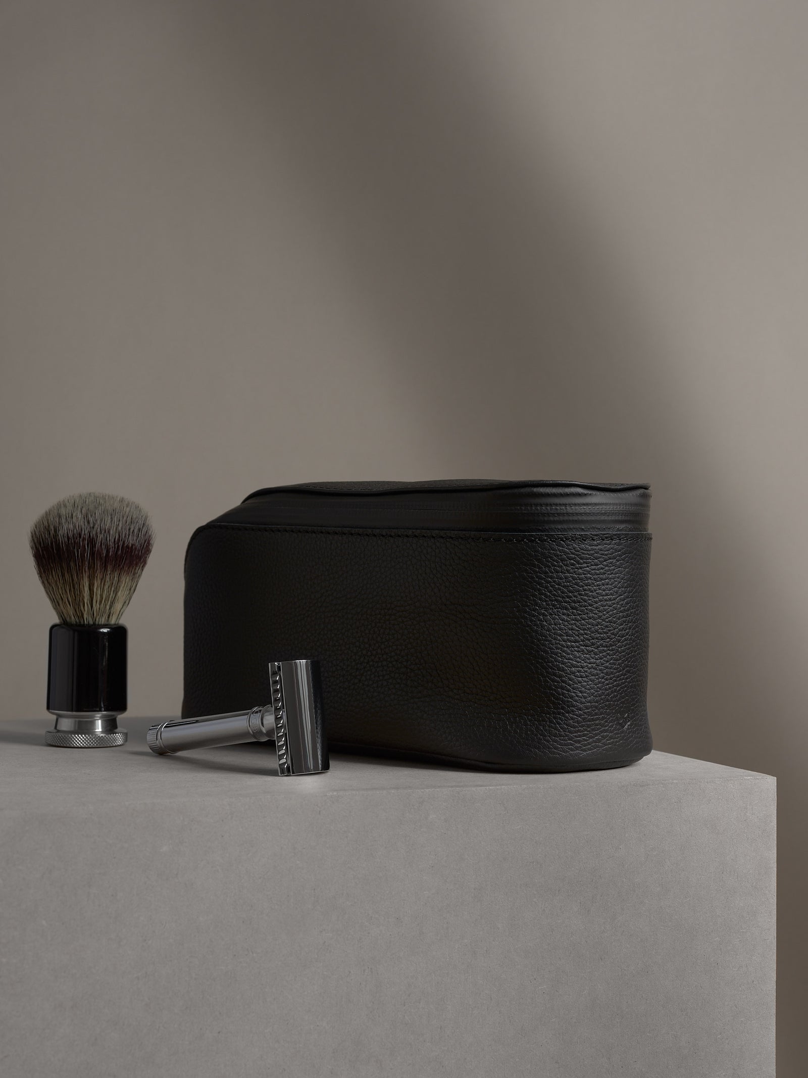 Black leather toiletry bag standing next to a classic safety razor and shaving brush.