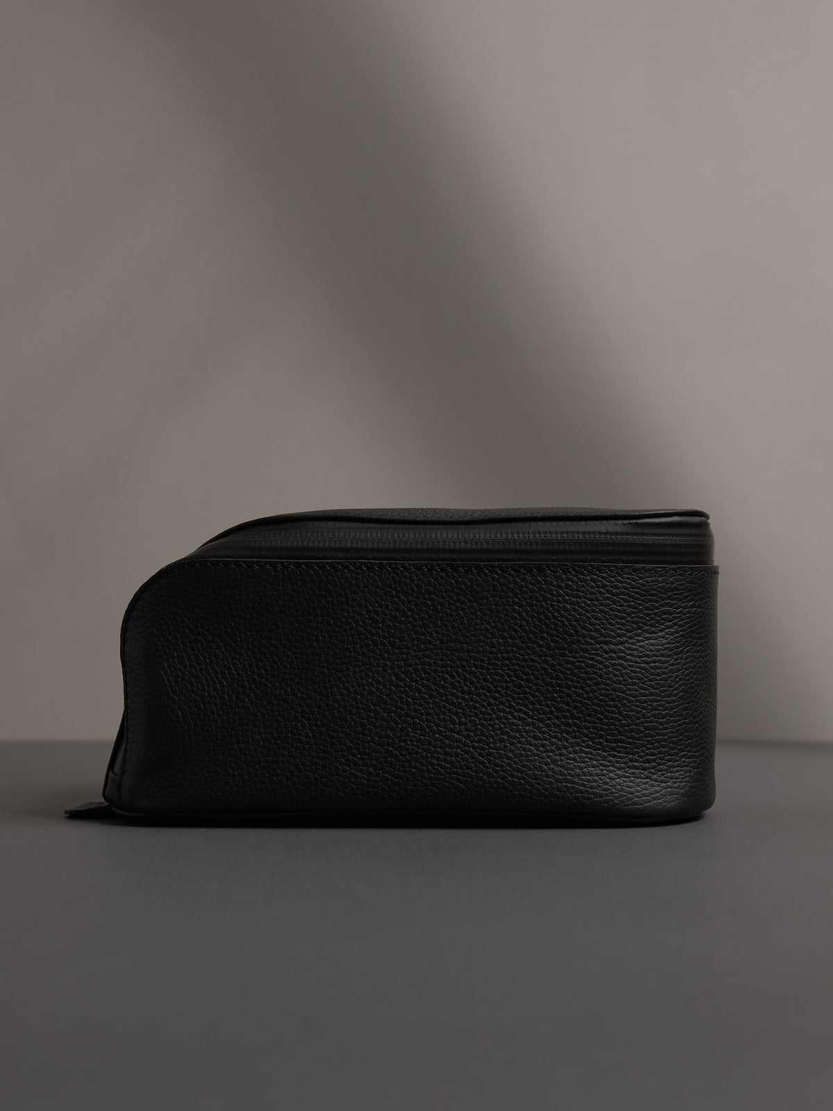 Full-side profile view of the black leather dopp kit, showcasing its capacity and structured shape.