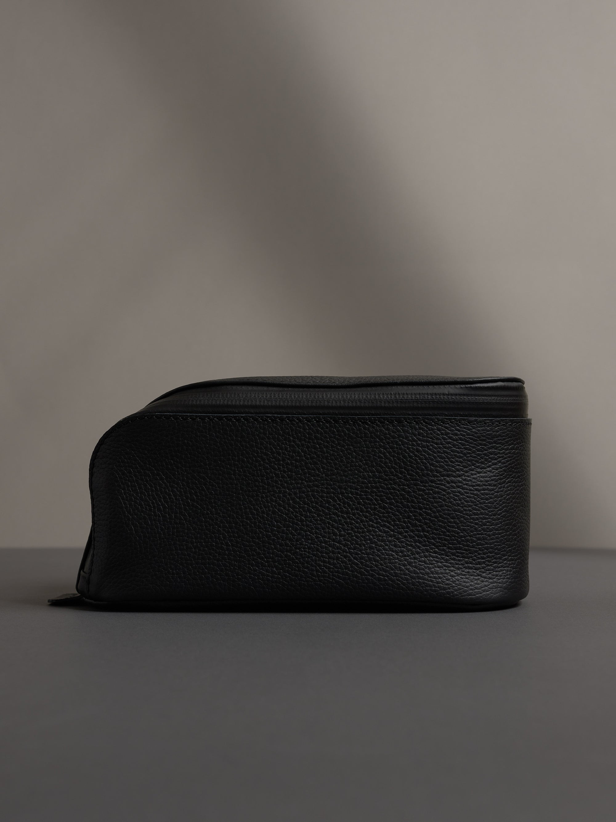 Full-side profile view of the black leather dopp kit, showcasing its capacity and structured shape.