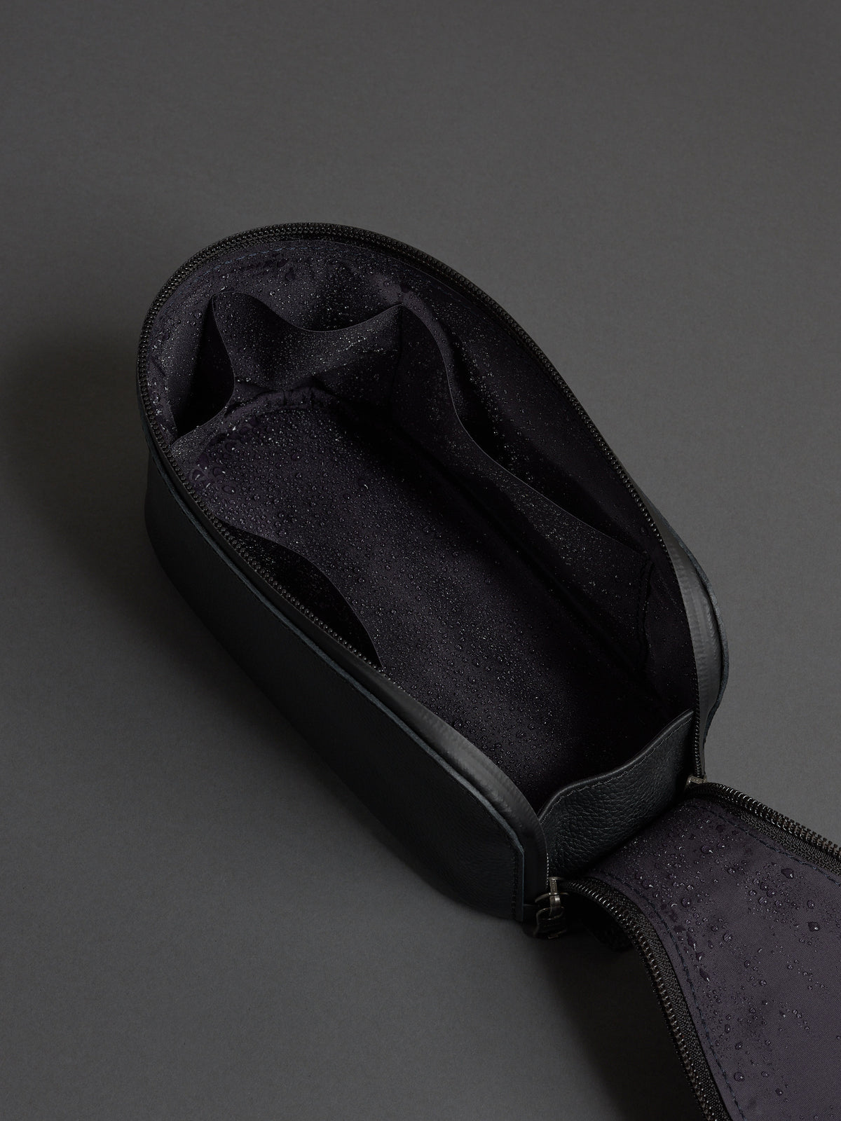 Open black leather dopp kit showing the water-resistant lining and internal organizational pockets.