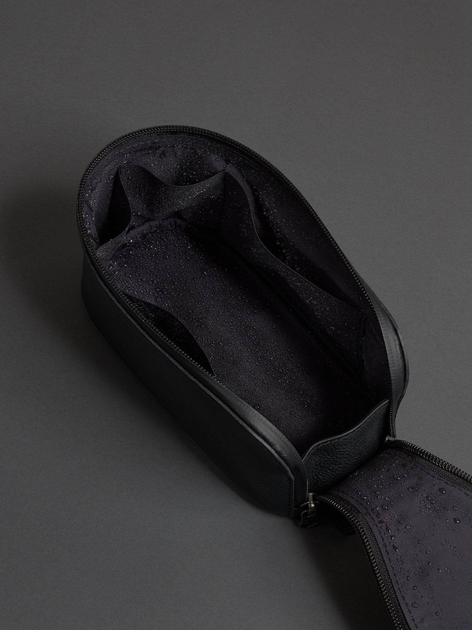 Open black leather dopp kit showing the water-resistant lining and internal organizational pockets.