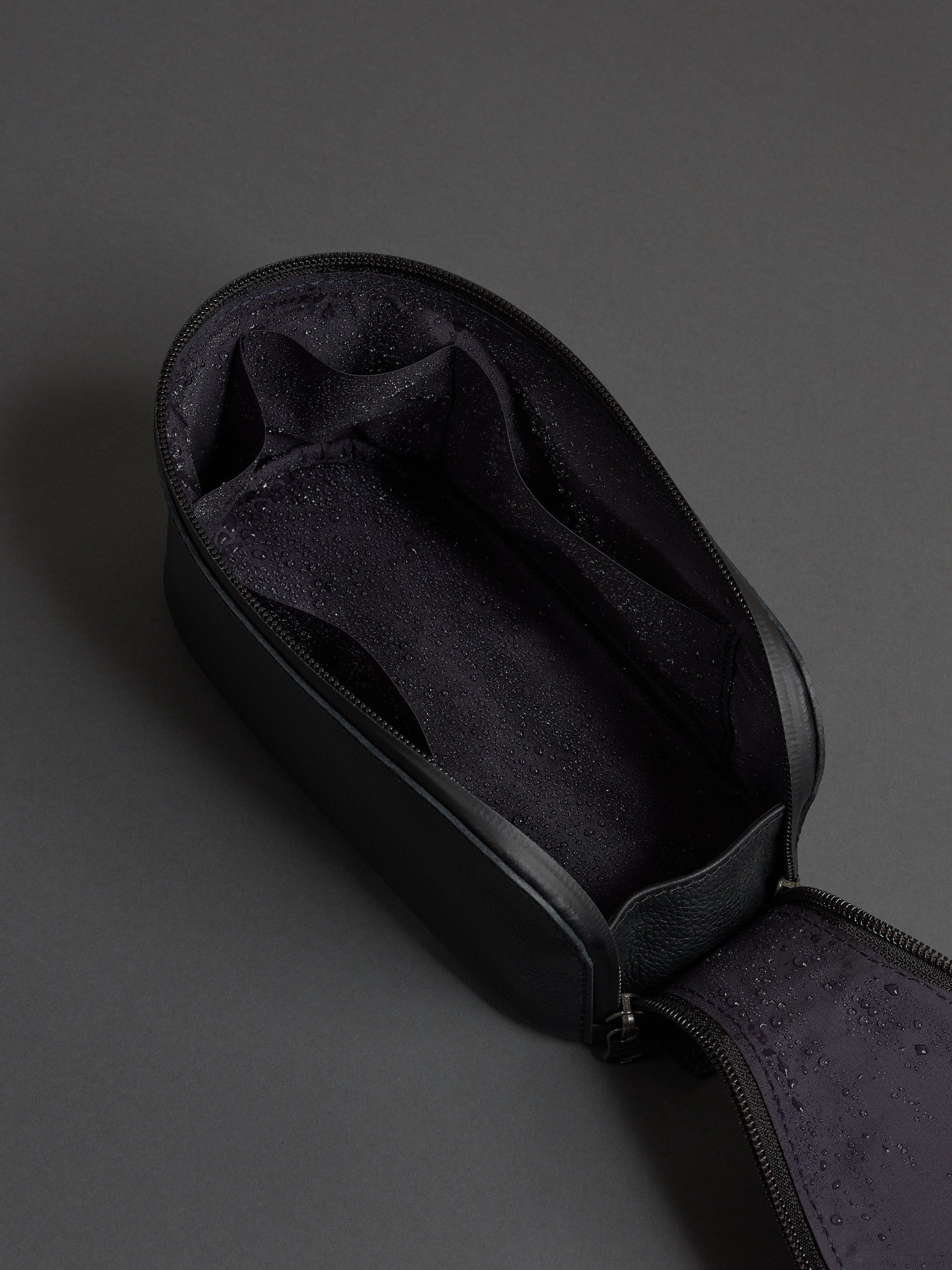 Open black leather dopp kit showing the water-resistant lining and internal organizational pockets.