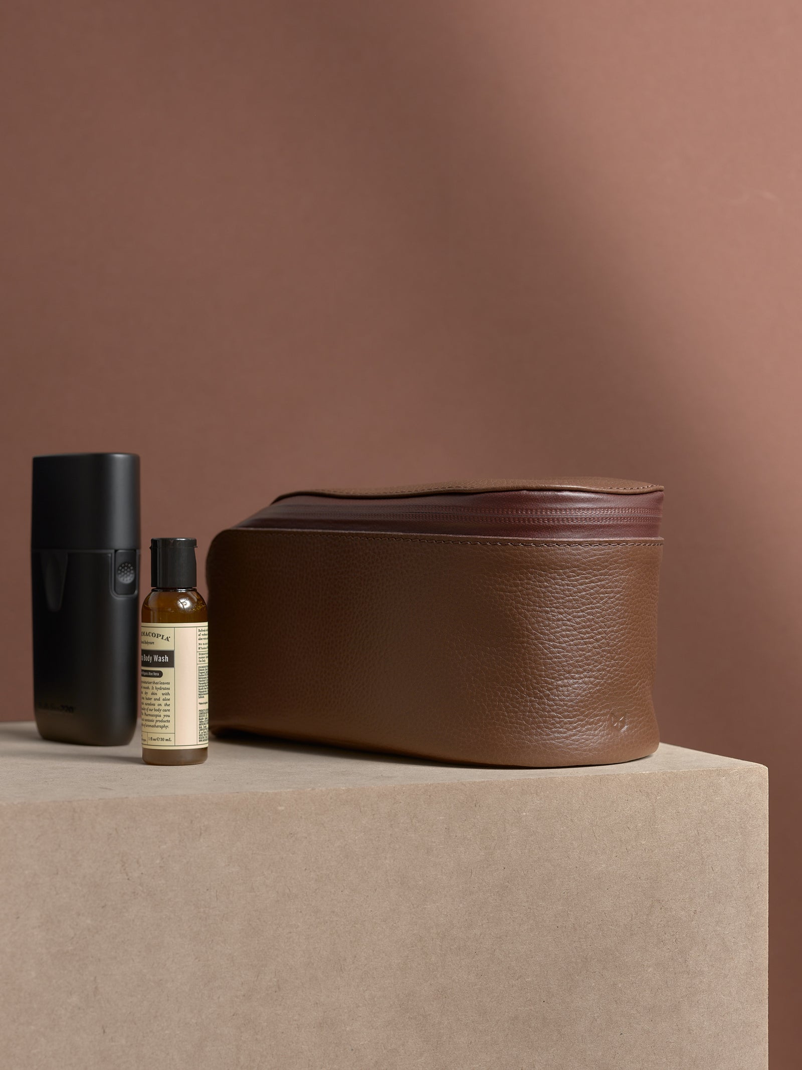 Closed tan Capra Leather Toiletry Bag standing next to an electric shaver.