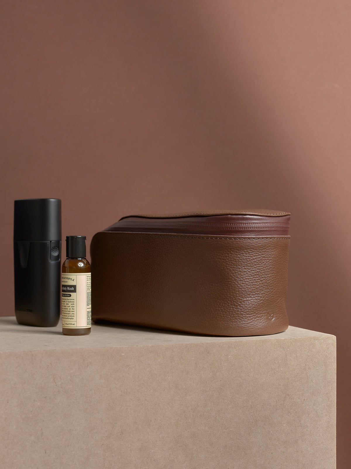Closed tan Capra Leather Toiletry Bag standing next to an electric shaver.