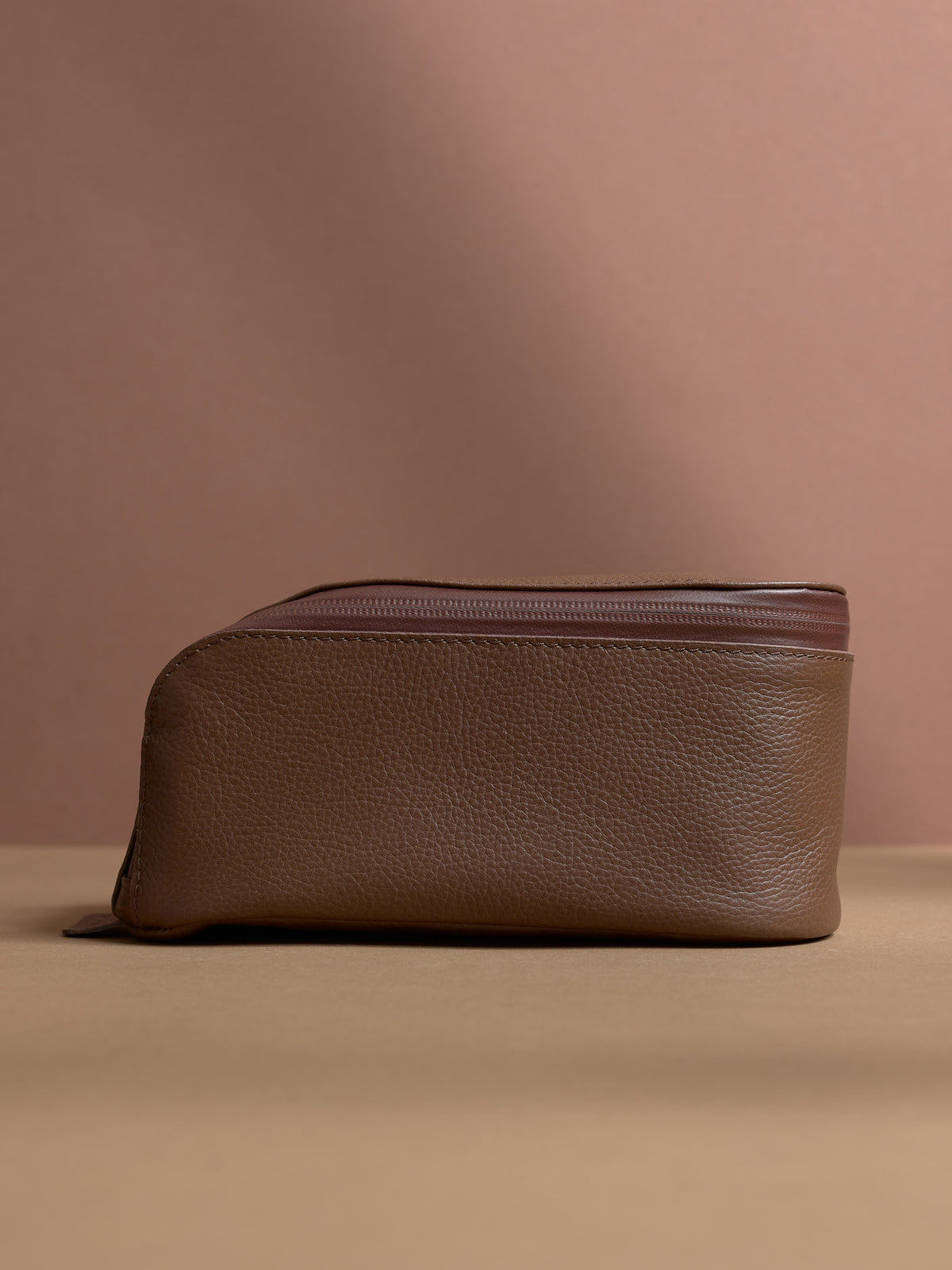 Side view of the closed tan Capra Leather Toiletry Bag, showing its curved profile.