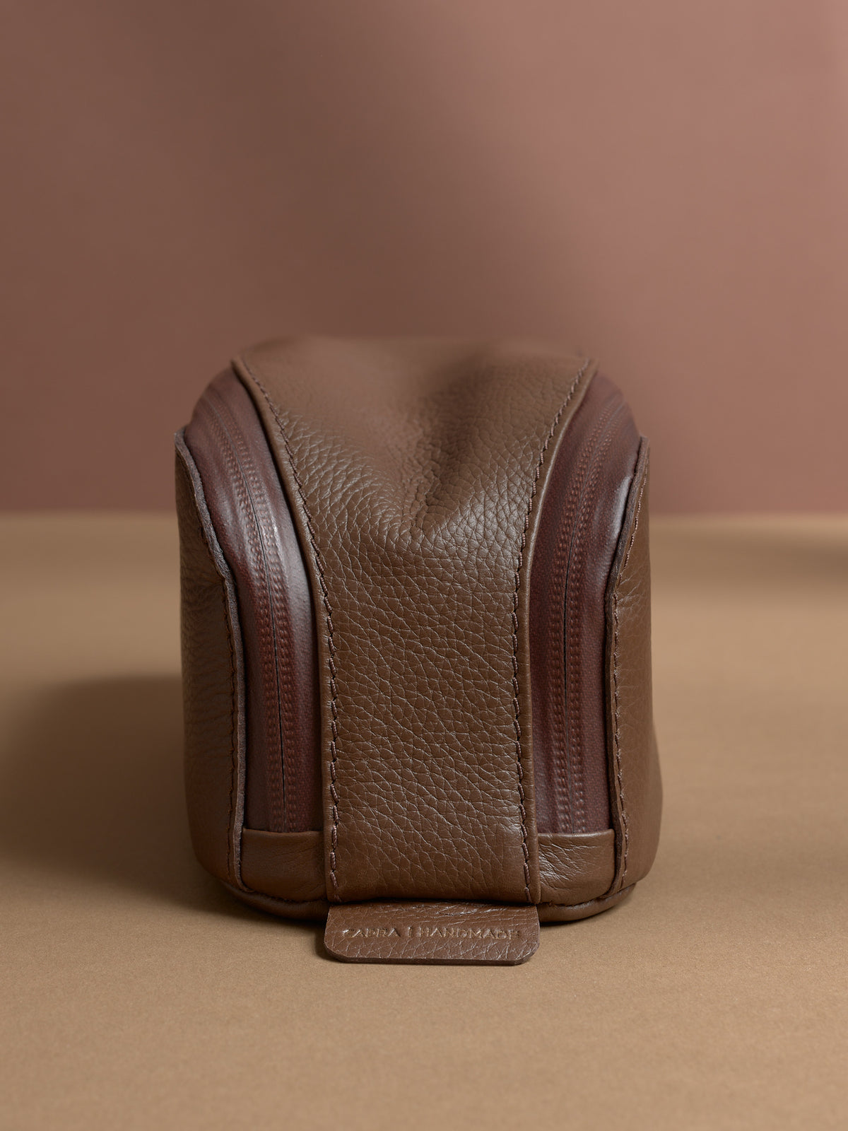 Front view of the vertical tan Capra Leather Toiletry Bag, highlighting twin zippers and stitching.